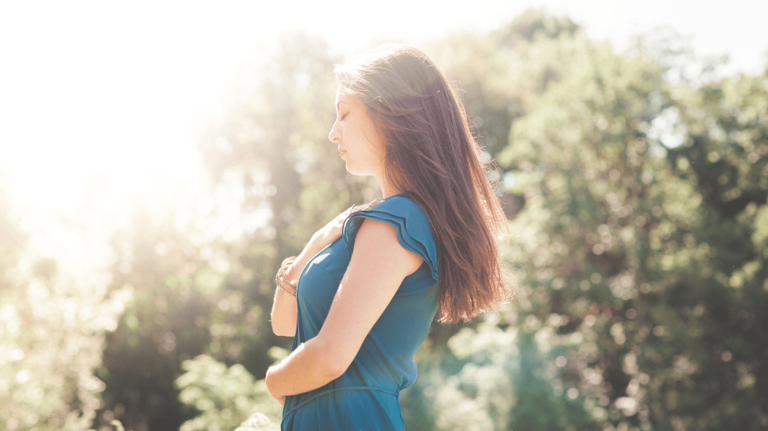 A women is holding her hands over her heart in nature with her eyes closed peacefully