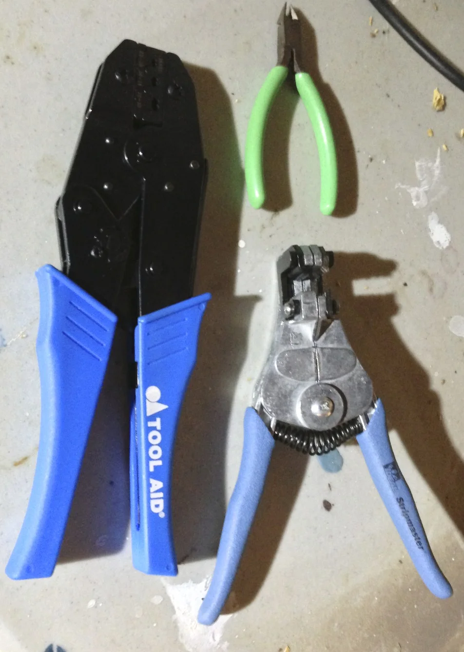 A ratcheting open barrel crimp tool (left). wire cutters (top) and wire strippers (bottom).