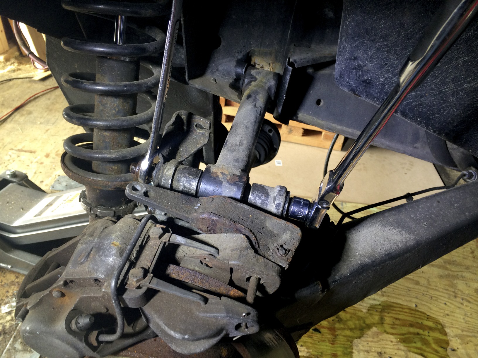 Two wrenches remove the nut and bolt from where the link arm meets the hub carrier.