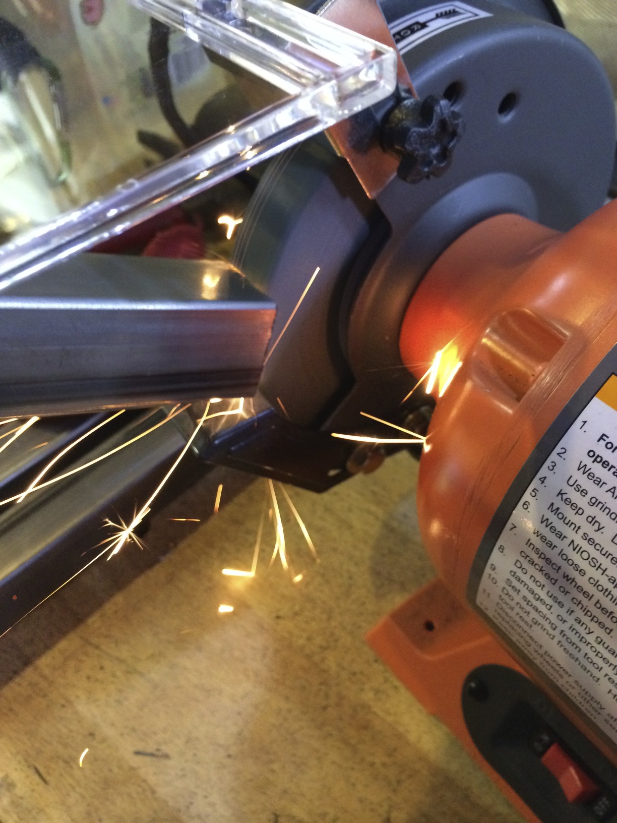 Grinding down the rough edges on a piece of square tubing.
