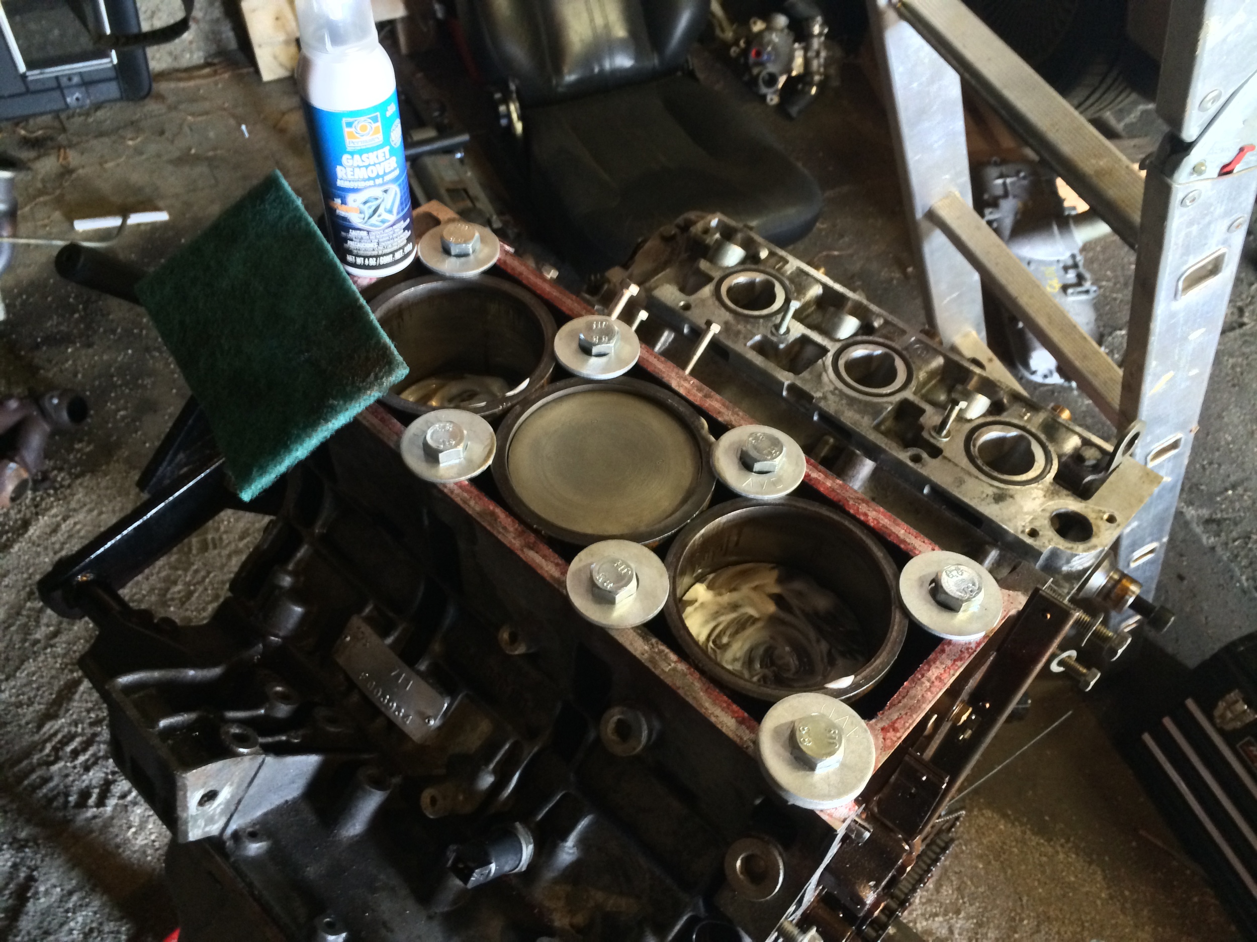 The cleaned-up center piston, and two dirty pistons, along with the Permatex Gasket Remover and a scrubbing pad.