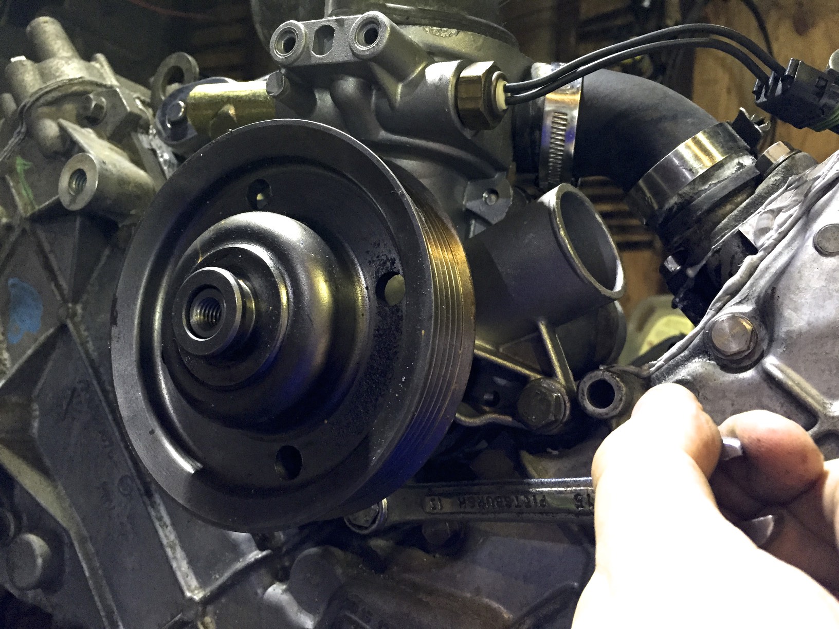 Using a box wrench to tighten the water pump bolt behind the pulley.