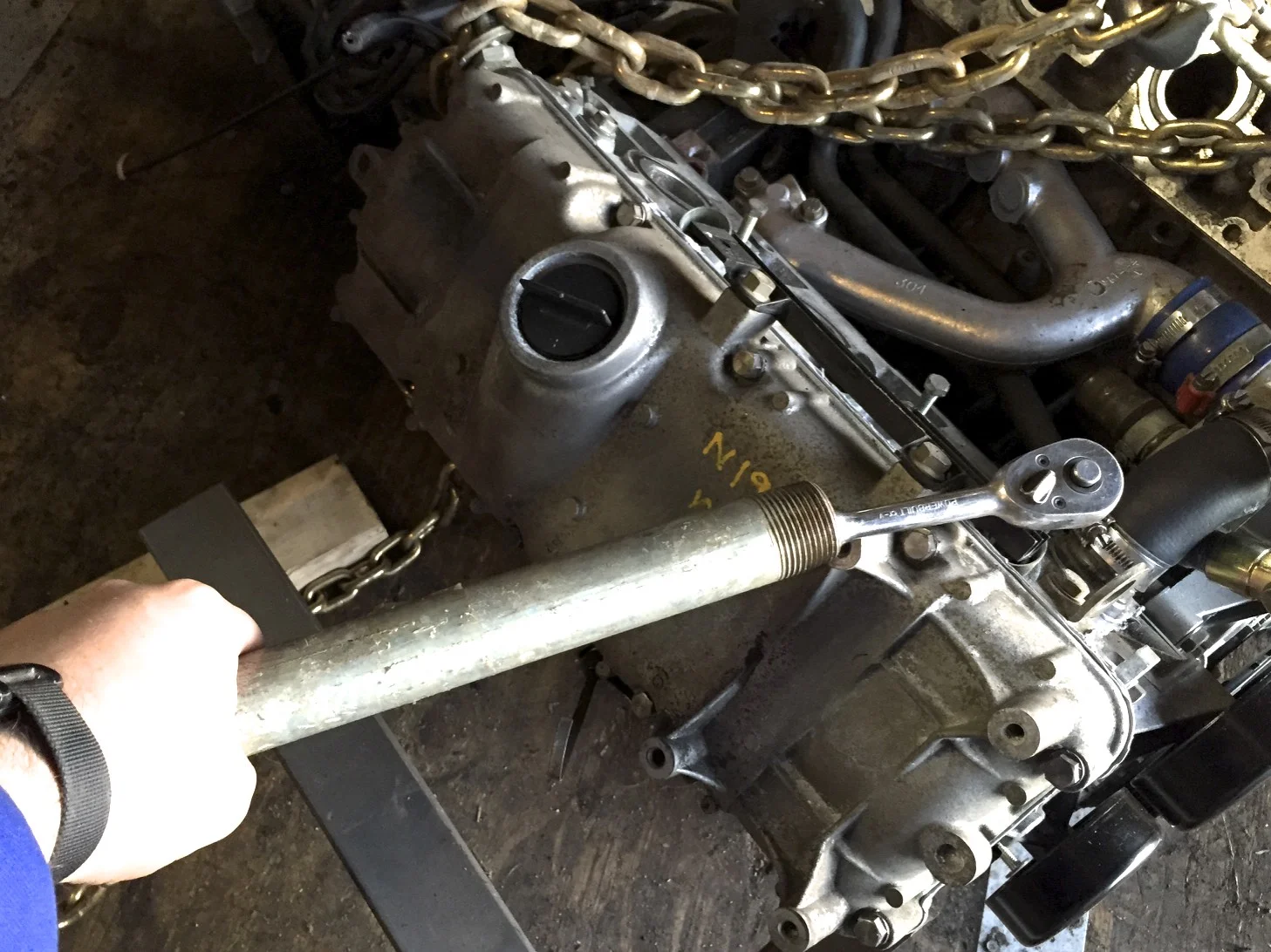 Using a pipe as a cheater bar on the end of a wrench to make it easier to remove a spark plug.