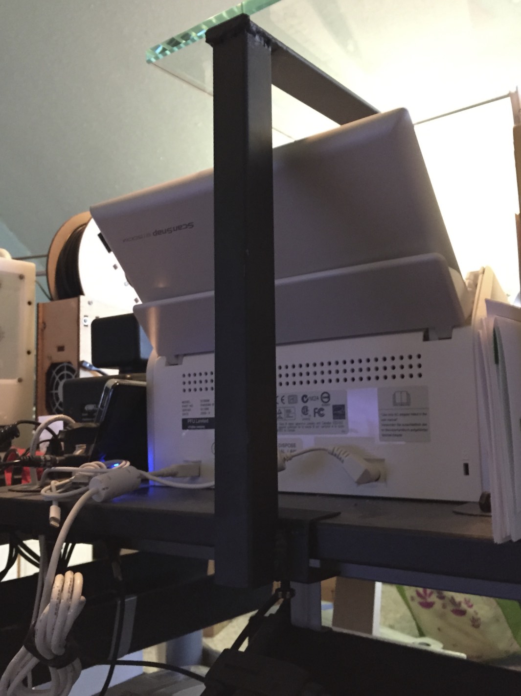 One of the mounts extending over my document scanner. The screw can be seen poking out under the mount, holding it to the desk.