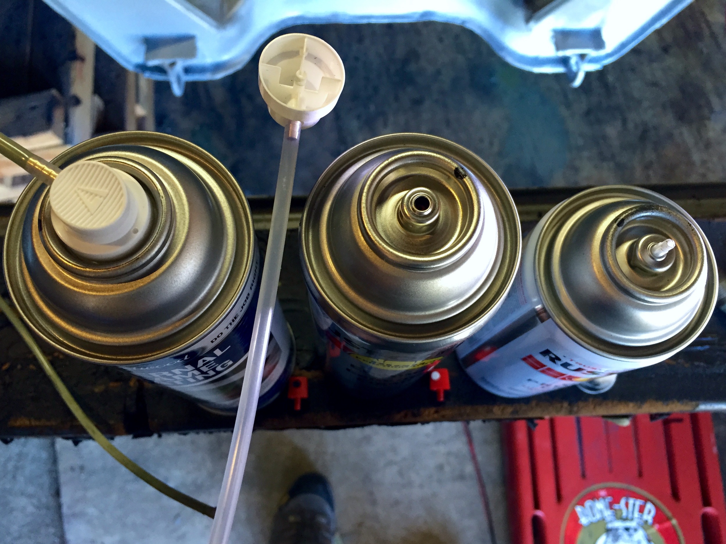 A top-down view of the cans. The middle can of Rustoleum can fit the extension wand (shown between the two left cans and on the leftmost Eastwood can). The rightmost can of Rustoleum has the wrong kind of nozzle, and the extension wand won't fit on it.