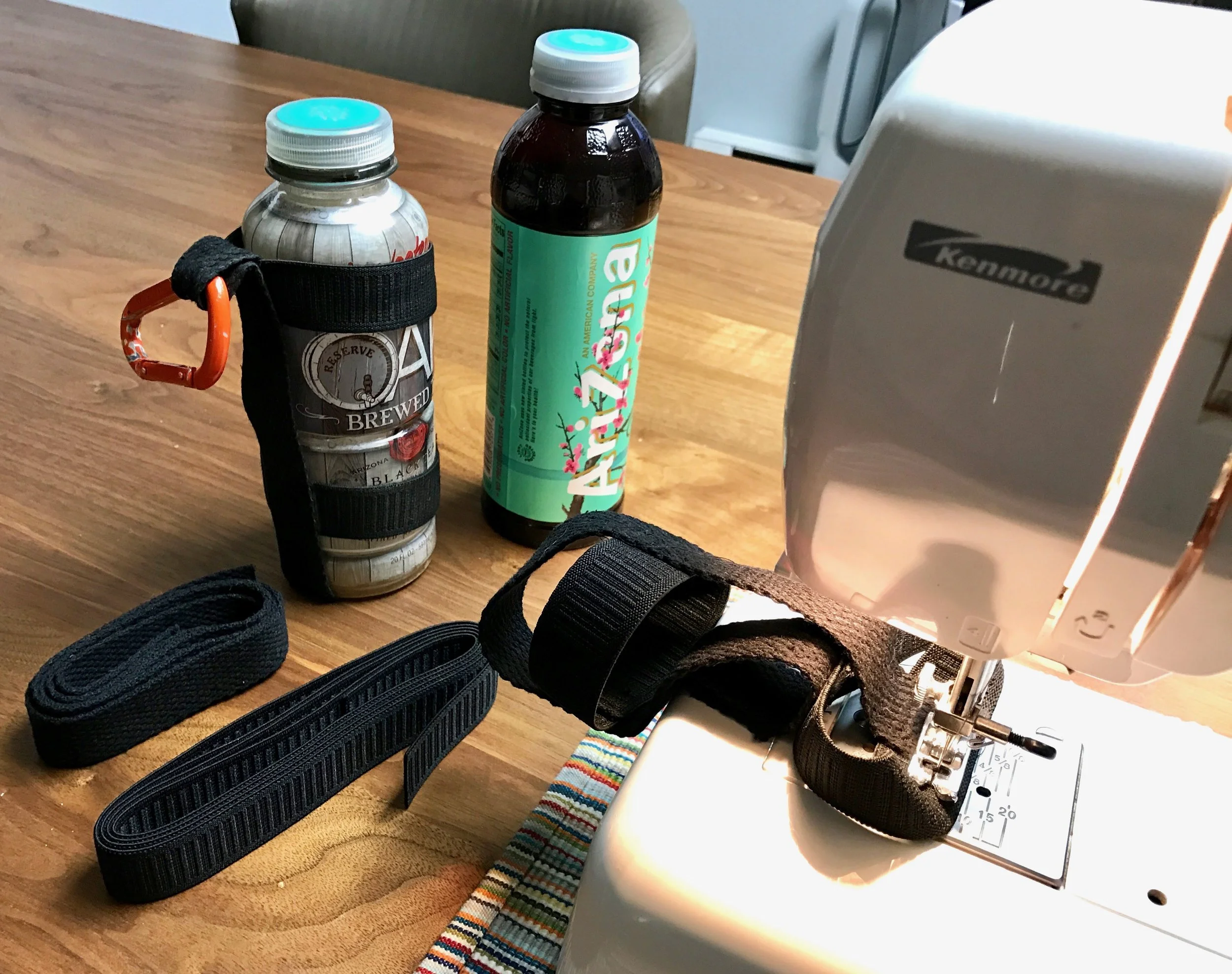 My original carrier on the old bottle, the bottle for the new carrier, some inelastic webbing, some elastic webbing, and the under-construction new carrier on the sewing machine.