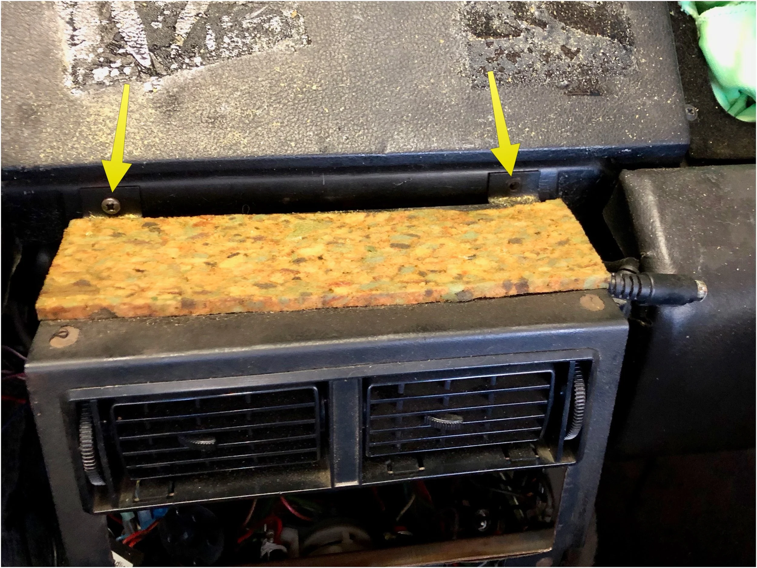 The yellow arrows point to the two screws that hold the center stack to the dashboard.