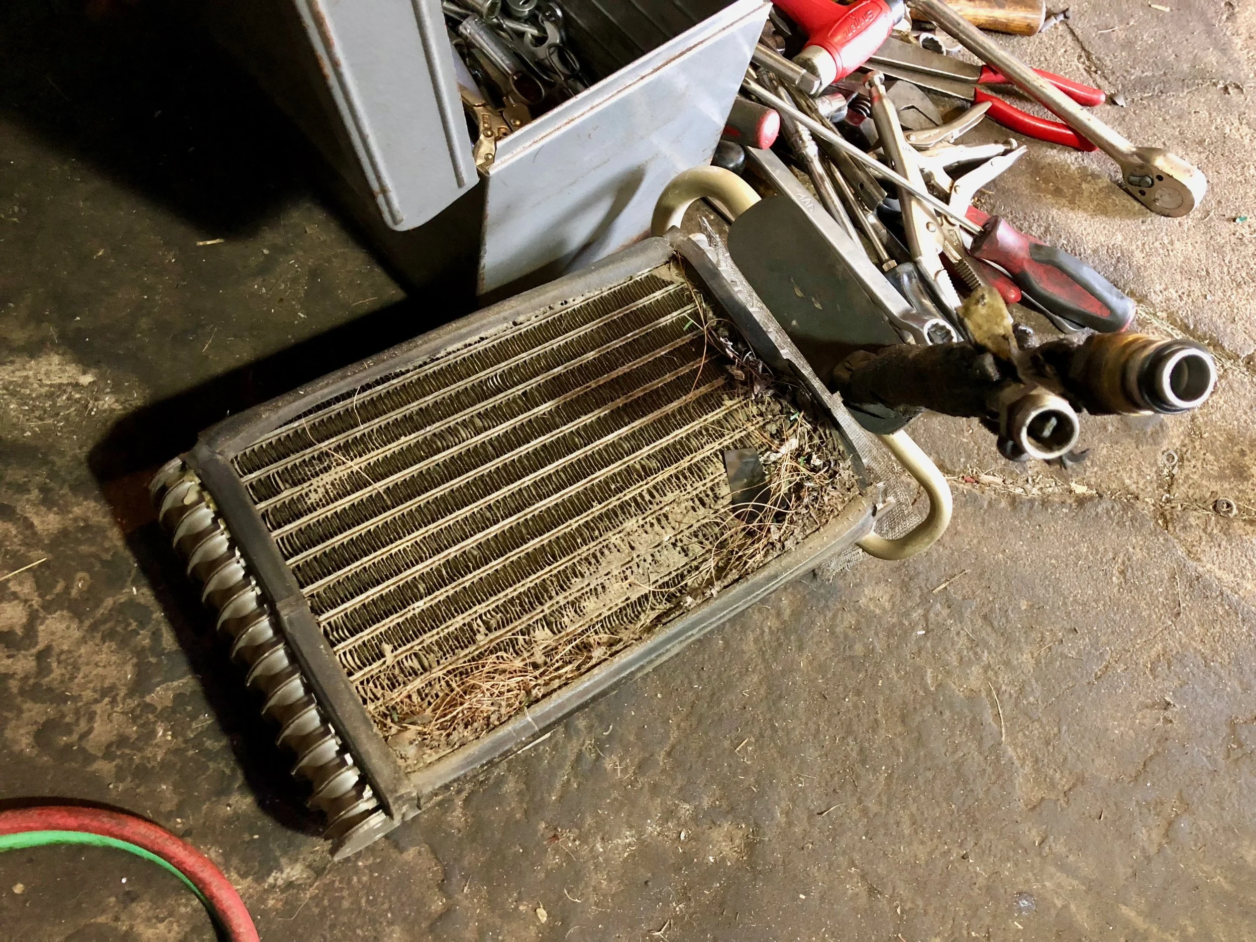 The old evaporator core removed from the box. There's a lot of debris on the bottom of the core. The orifice tube can be seen still inside the near pipe.