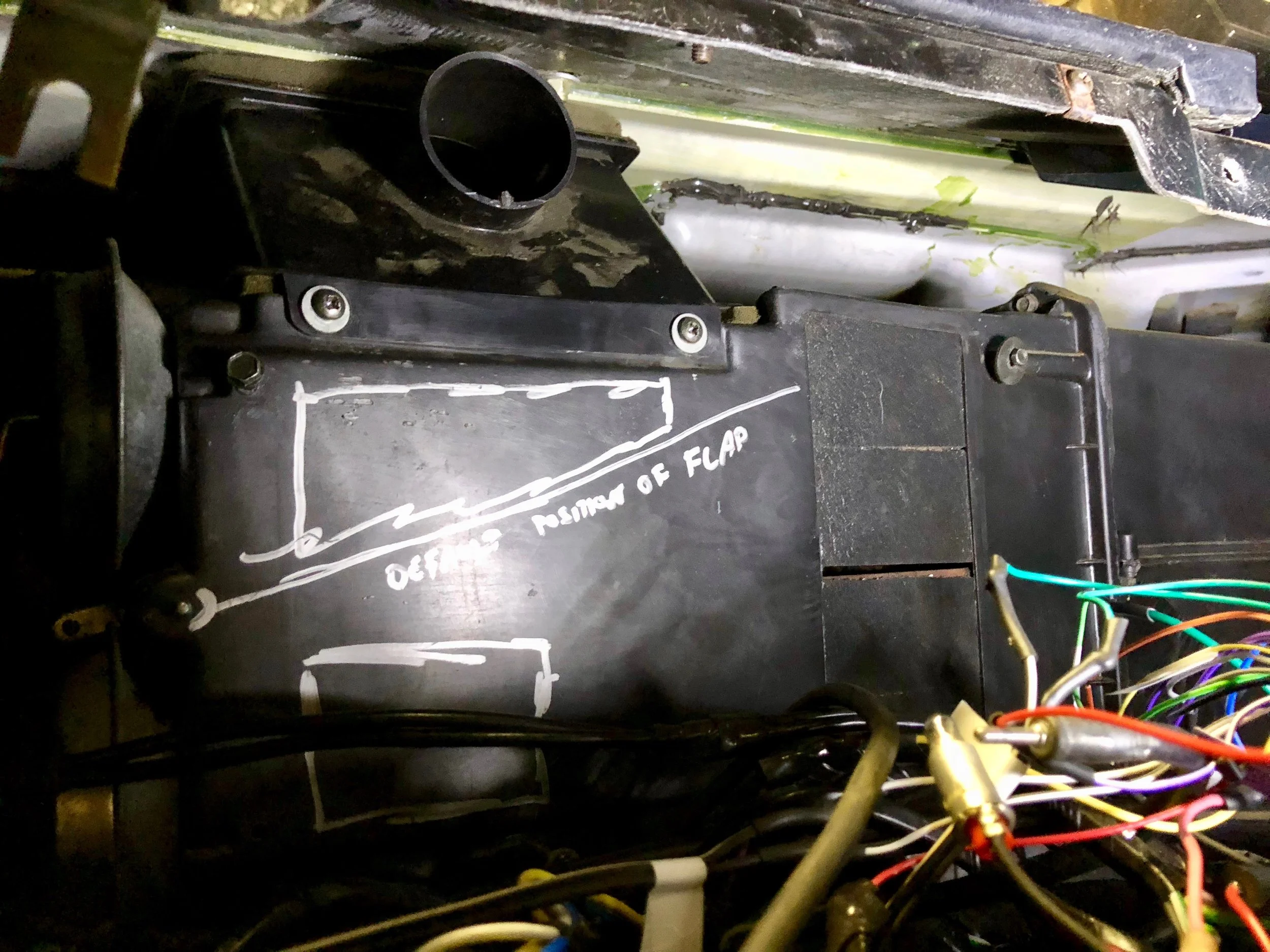 The position of the defrost vent under the dash. The two screws on the face come out, and then it can be tilted out from under the dash. The air distributor is removed in this picture, as is the duct that goes from the distributor to the vent. The drawings on the box are for a later experiment, and indicate safe areas to cut the box and the default location of the defrost flap.