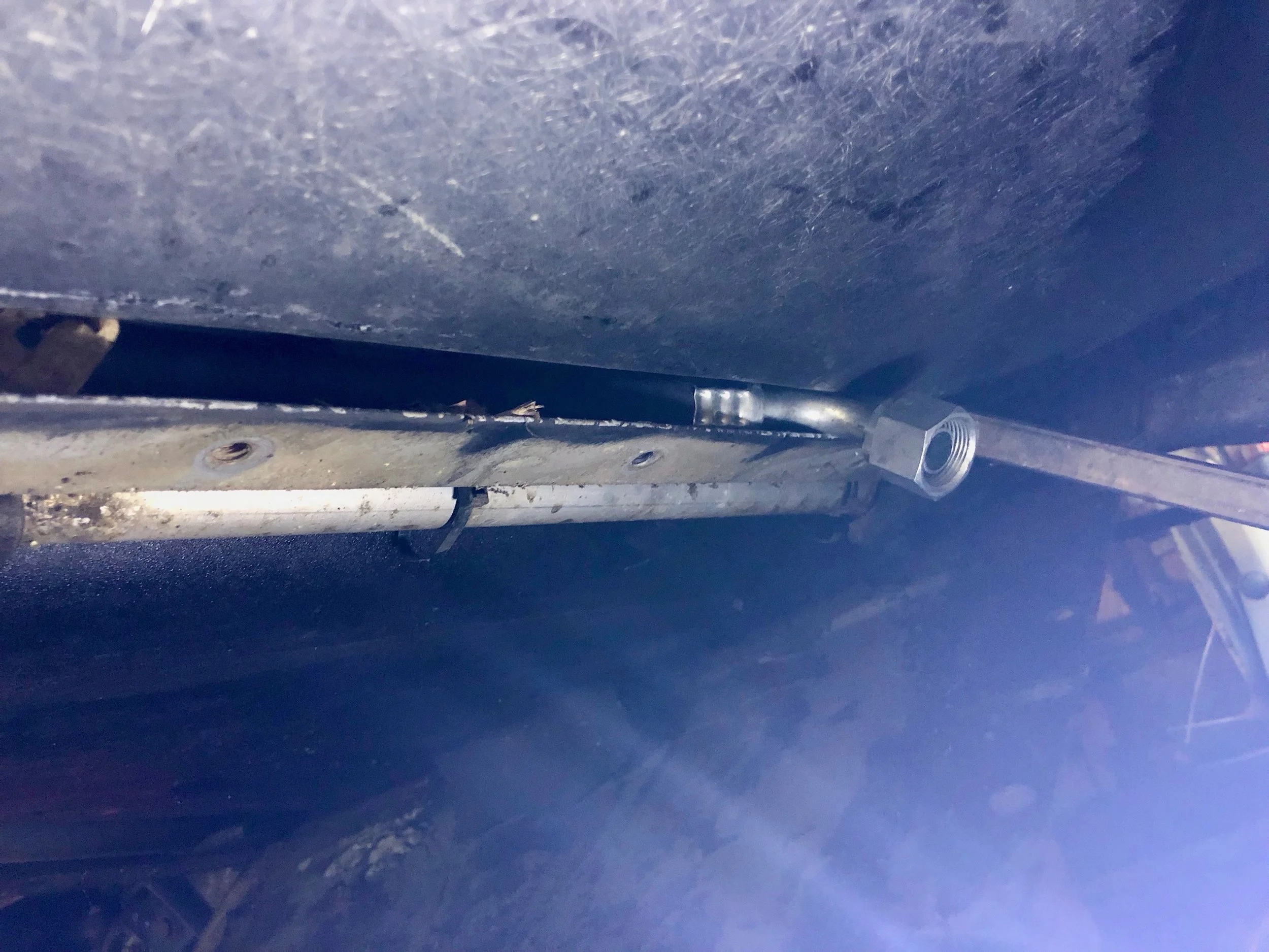 The hose connector peeking out of the space between the frame and body as we run it towards the front of the car. The bend in the connector very tightly fits through the gap. The metal bar visible behind the connector was being used as a wedge to pry the frame and body apart.