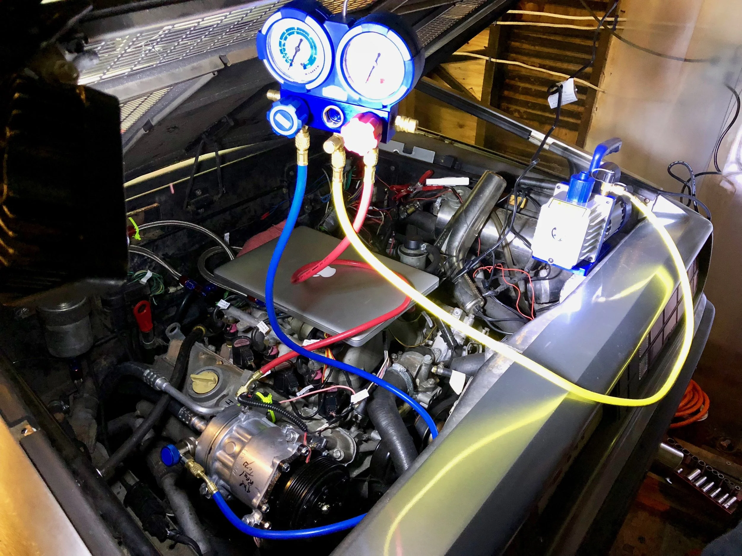 The manifold and gauges hooked up to the A/C lines at the compressor, and a vacuum pump running to pull vacuum on the system.