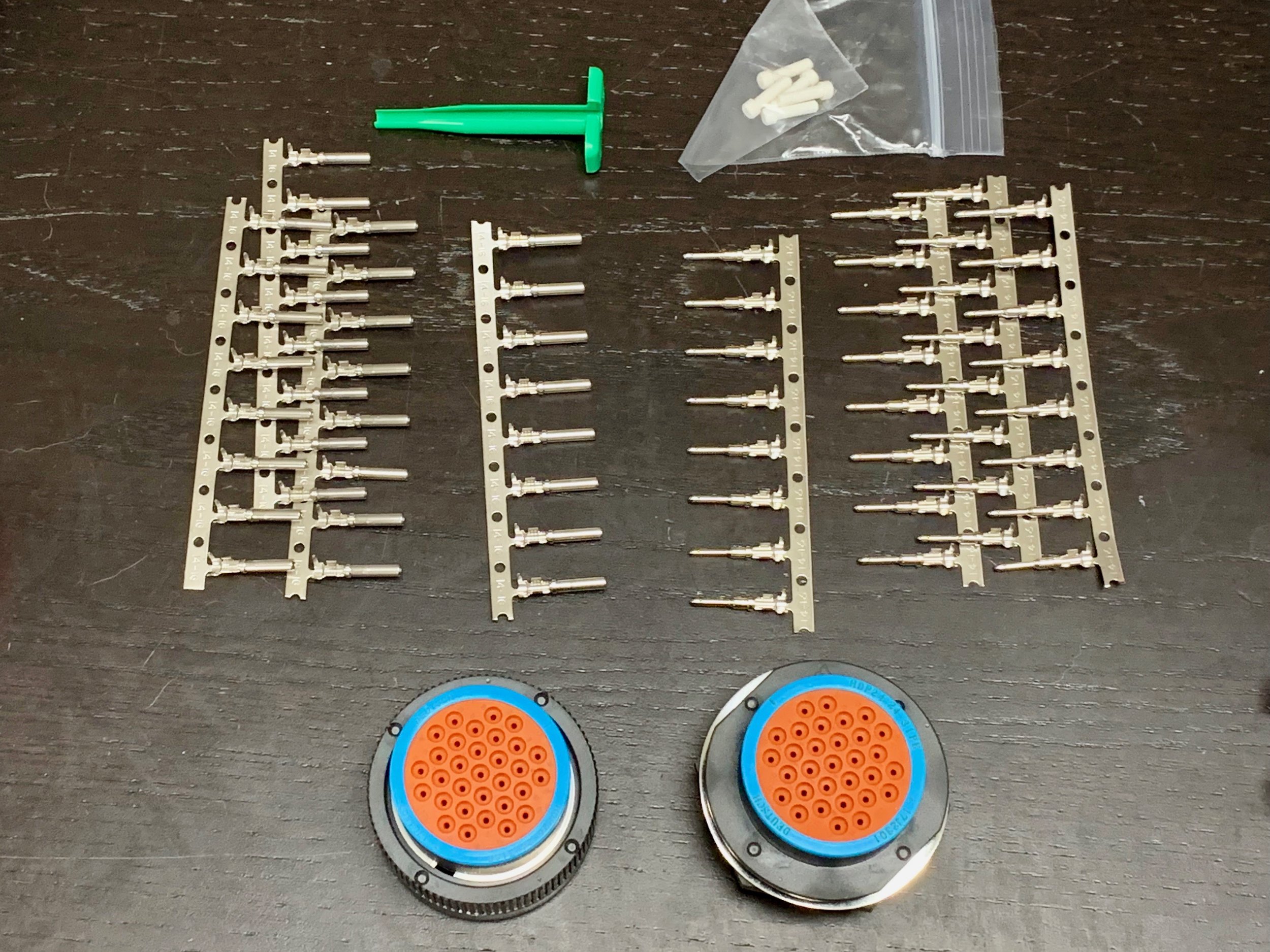 Both halves of the connector, stamped pins, green removal tool, and white plugs.