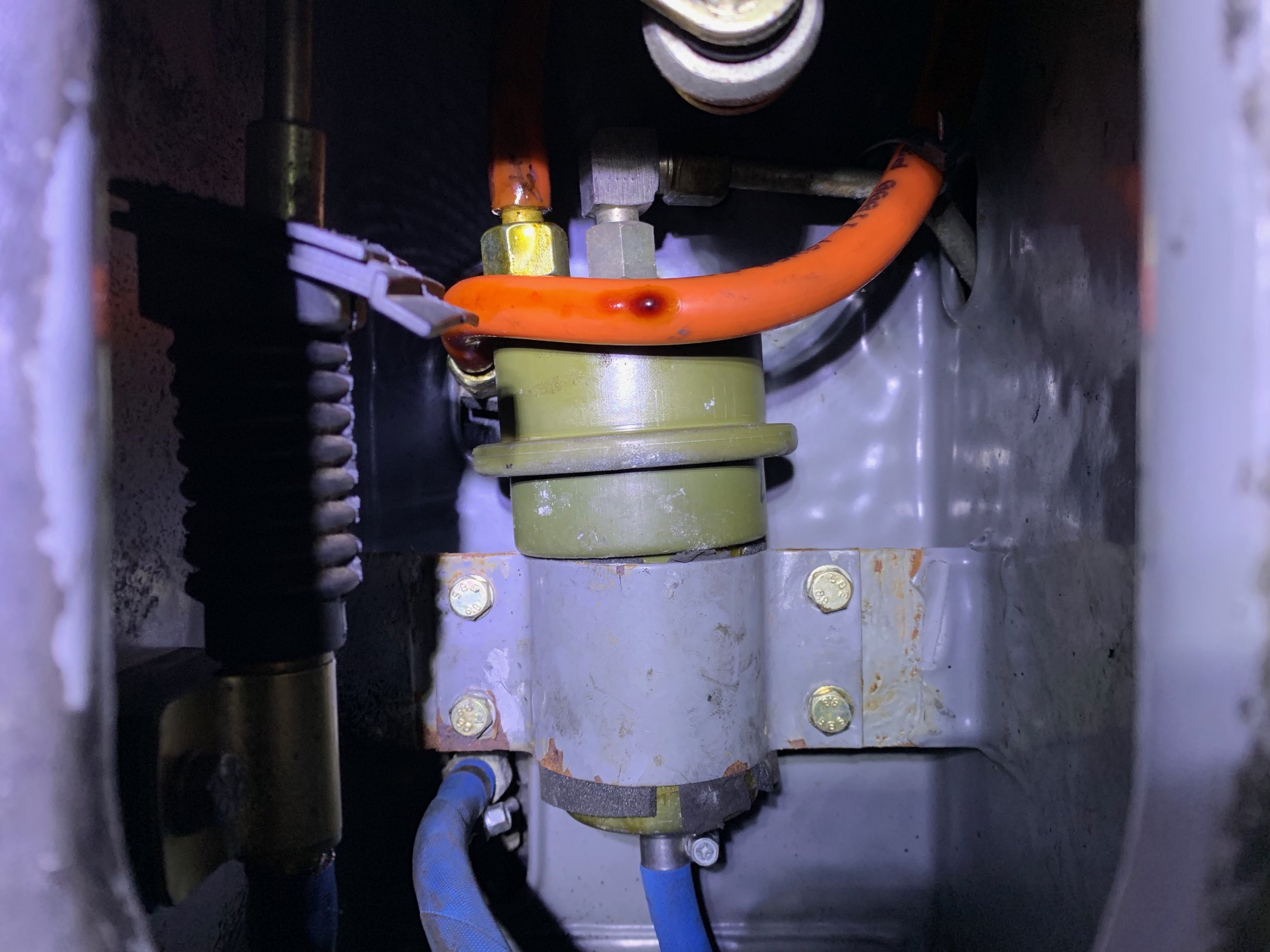 The fuel accumulator nested in the center of the frame, with some drips of leaking fuel on it. The very end of the bell crank lever is visible at the top of the picture, and the cable running to the transmission on the left side.