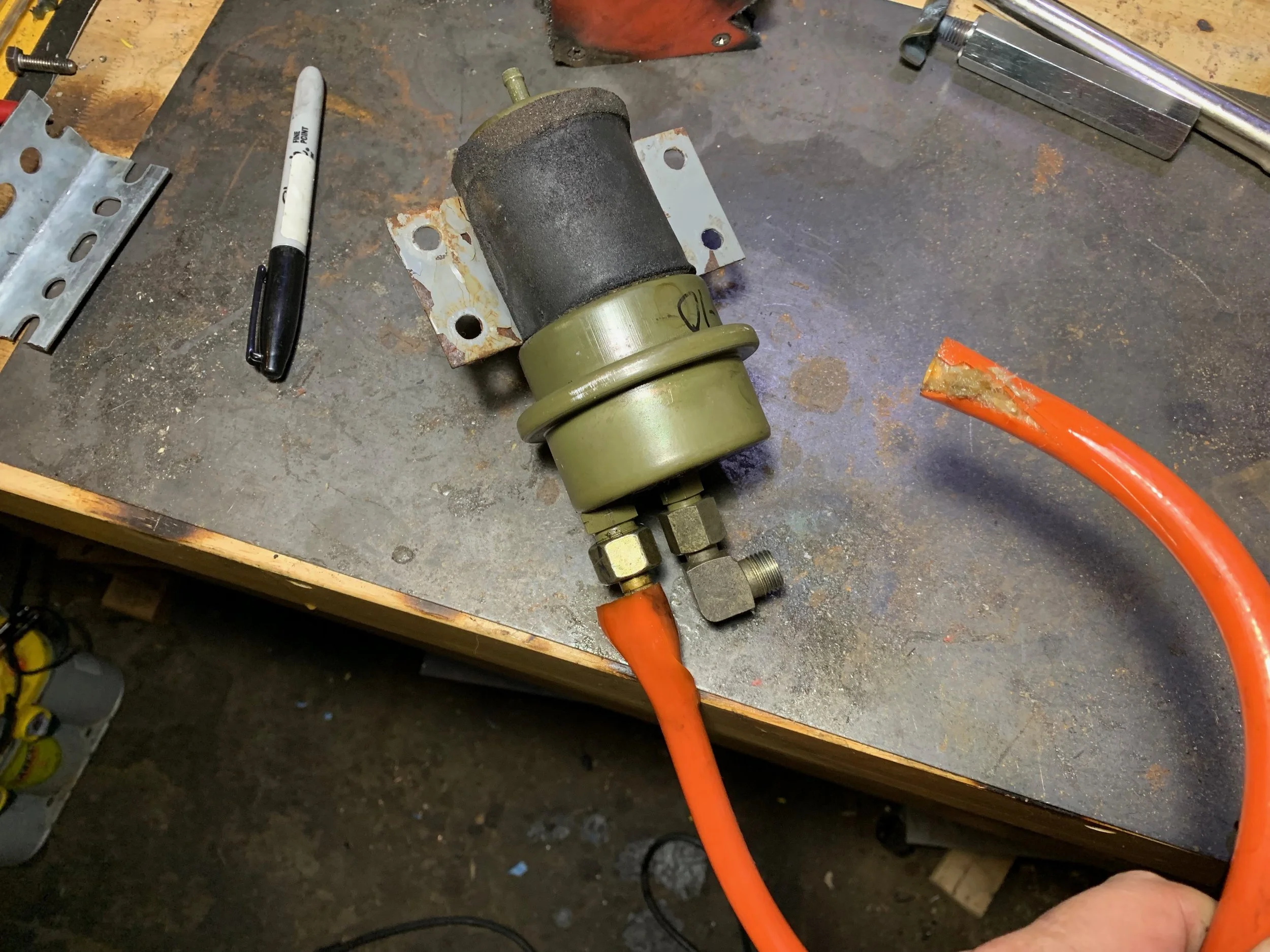 The accumulator removed from the car. One end of the orange hose is partially cut for removal, while the other end was cut off in the car.