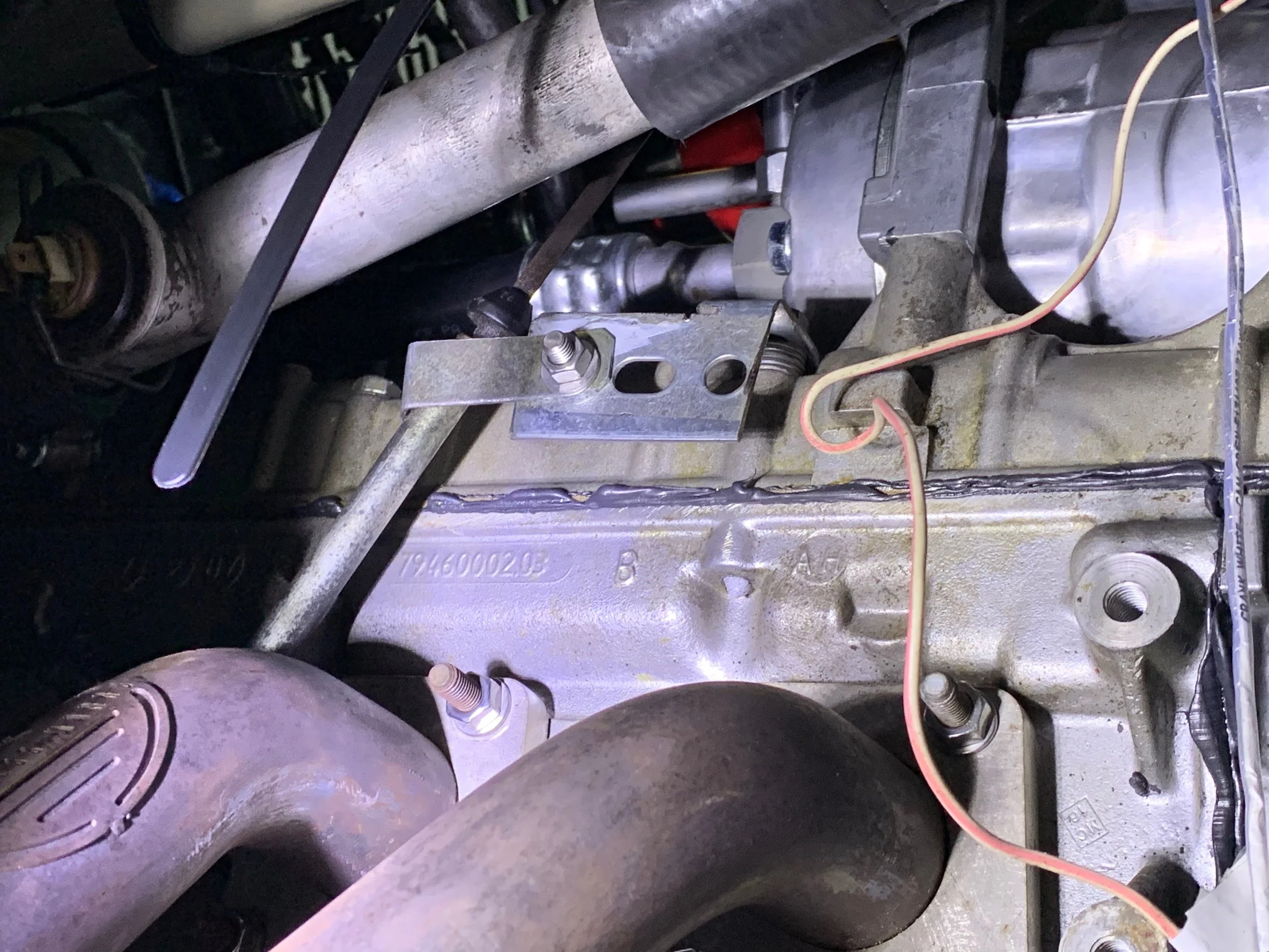The dipstick tube attached to the bracket, which is then attached to a valve cover bolt behind the A/C compressor, supported by a stack of washers.