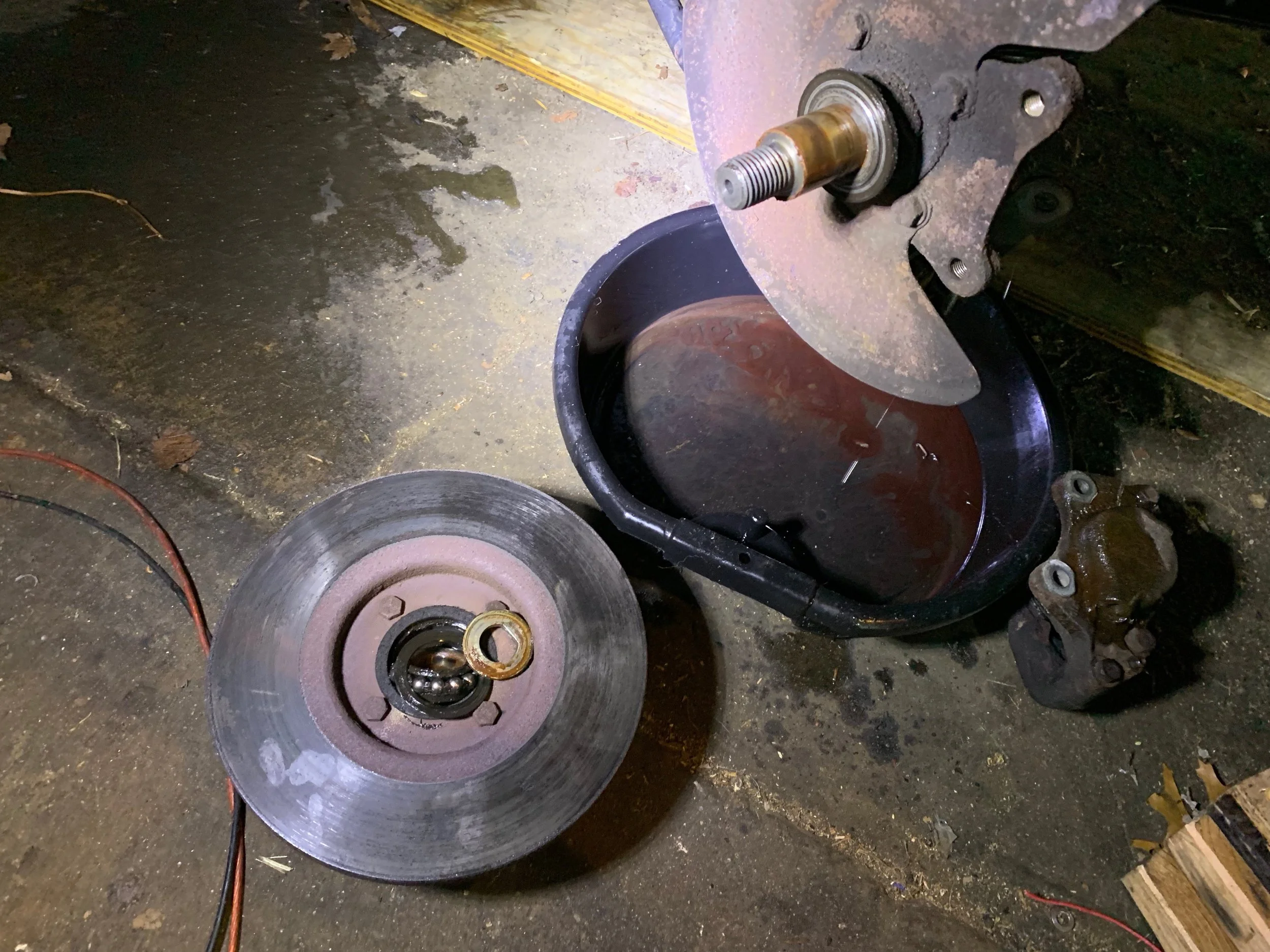 The hub and rotor after being removed. You can see how the bearing fell apart inside the center of the hub. Be sure to keep the spacer washer (visible lying on the rotor). The caliper is lying on the ground next to the pan.