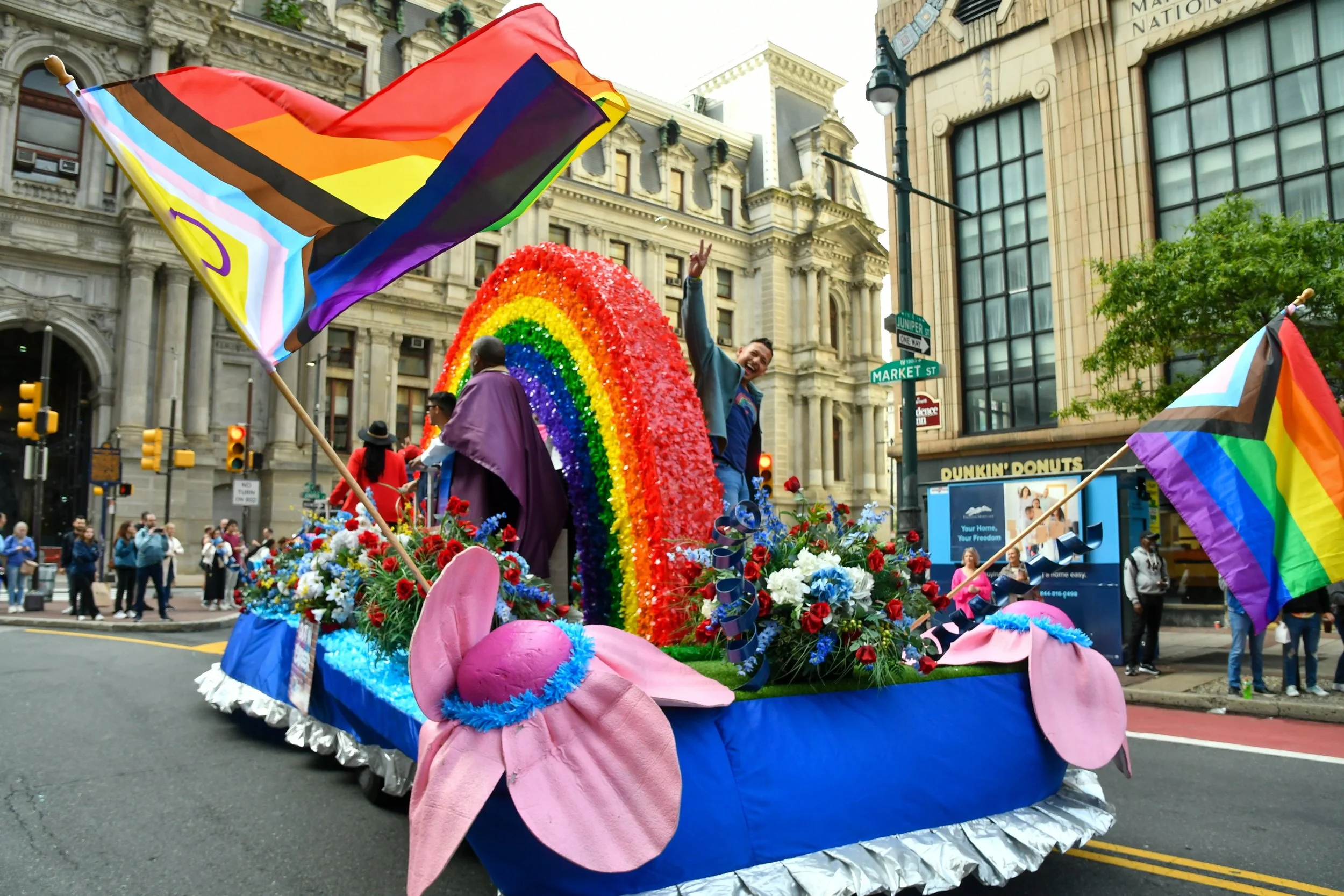 Blue parade float with rainbow design and inclusive rainbow pride flags