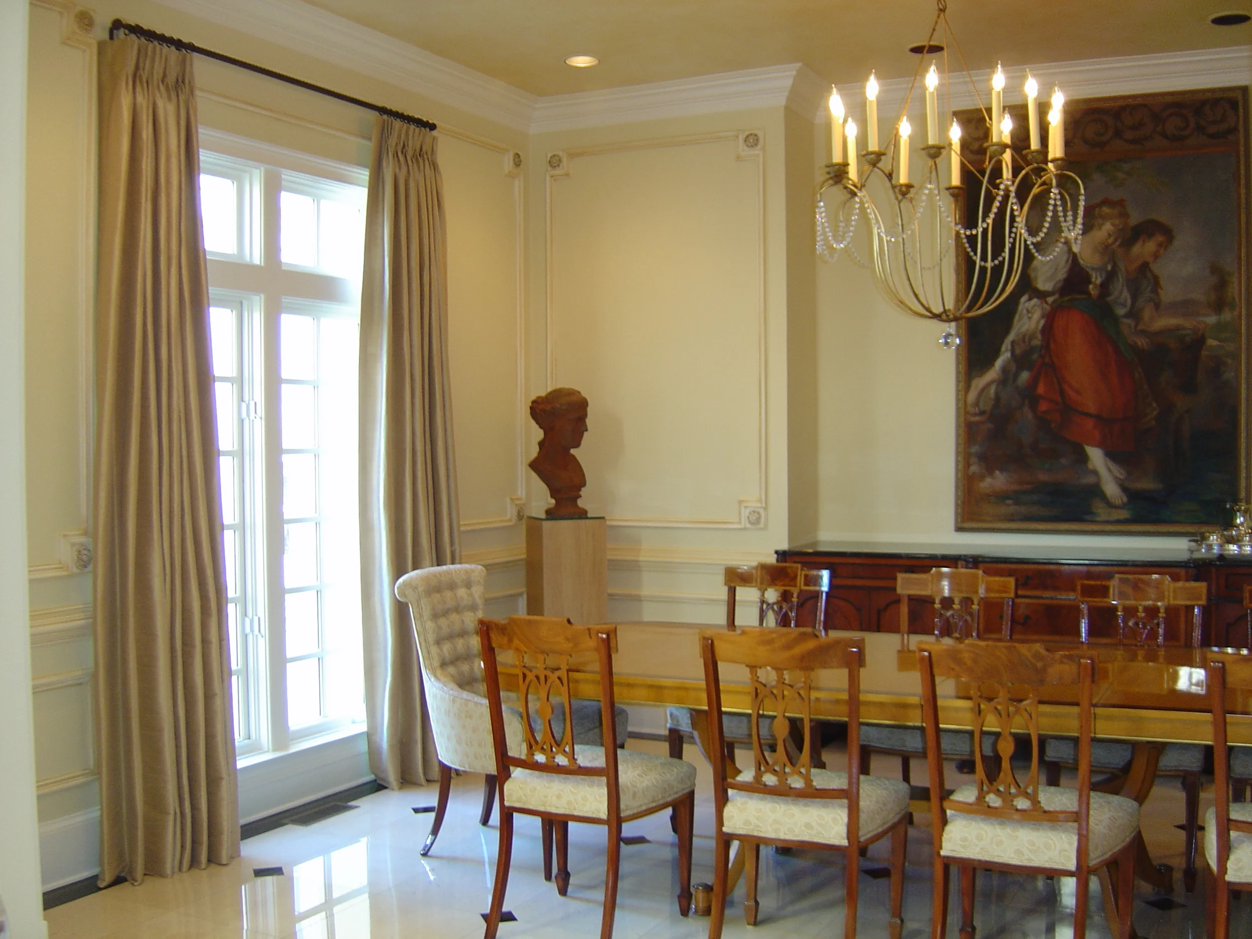  To transform the dining room from a traditional space to being more transitional in feel, the applied molding and ceiling were painted with a metallic finish. &nbsp;The chandelier, drapery, and head chairs were added. &nbsp;The existing dining table