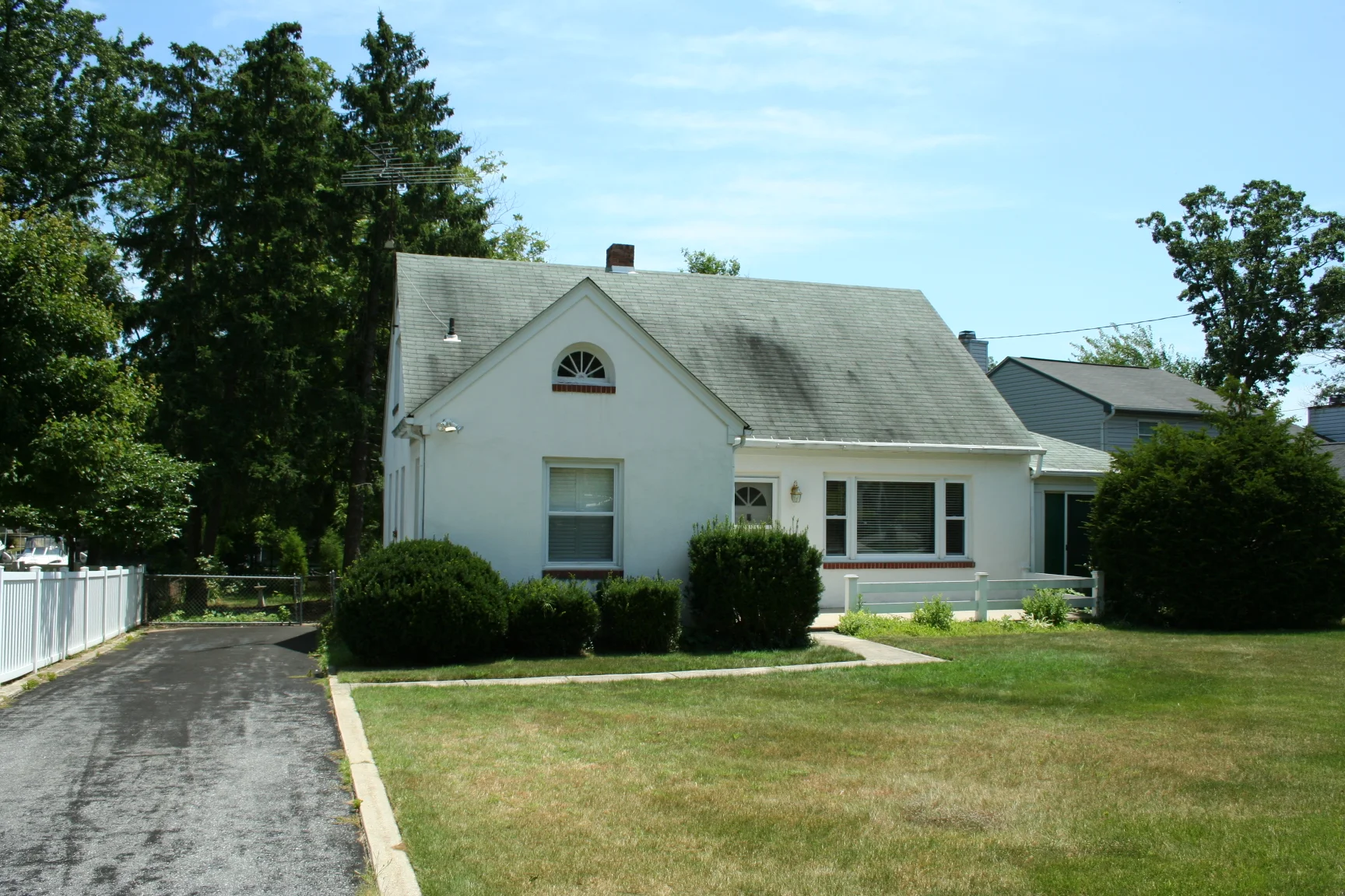 Before: the front of a modest one-story block home, with stucco, on a deep lot waterfront lot.