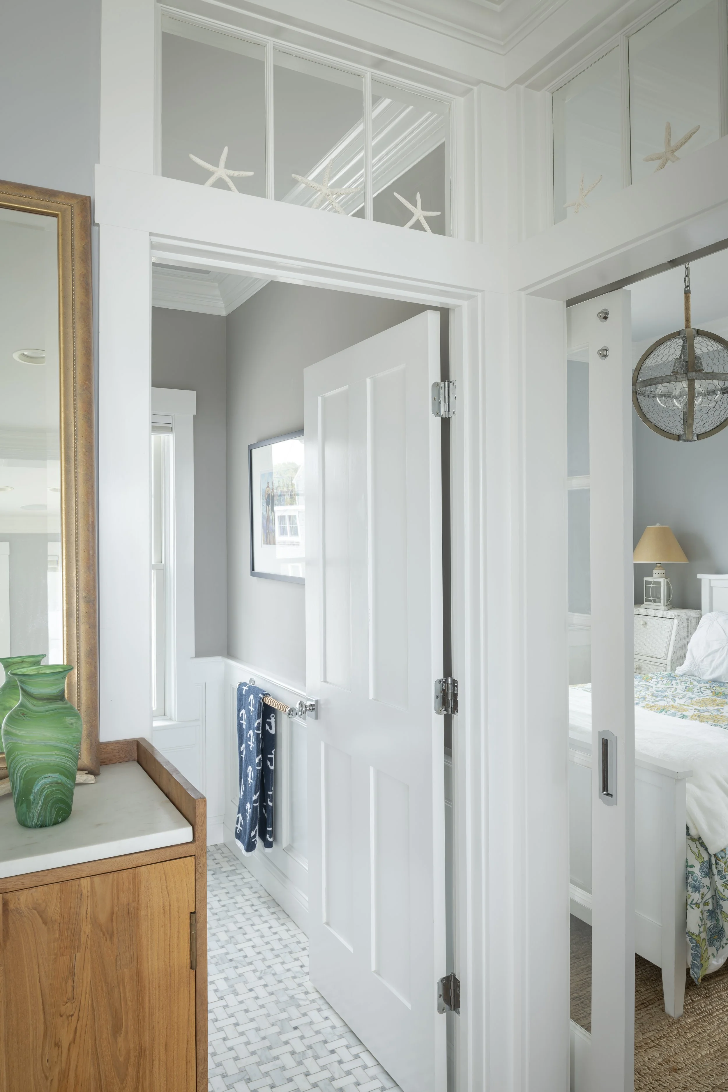 Interior view of a bright, white-painted home with a doorway leading to a bedroom, decorated in a coastal style with starfish accents and nautical-themed towels.