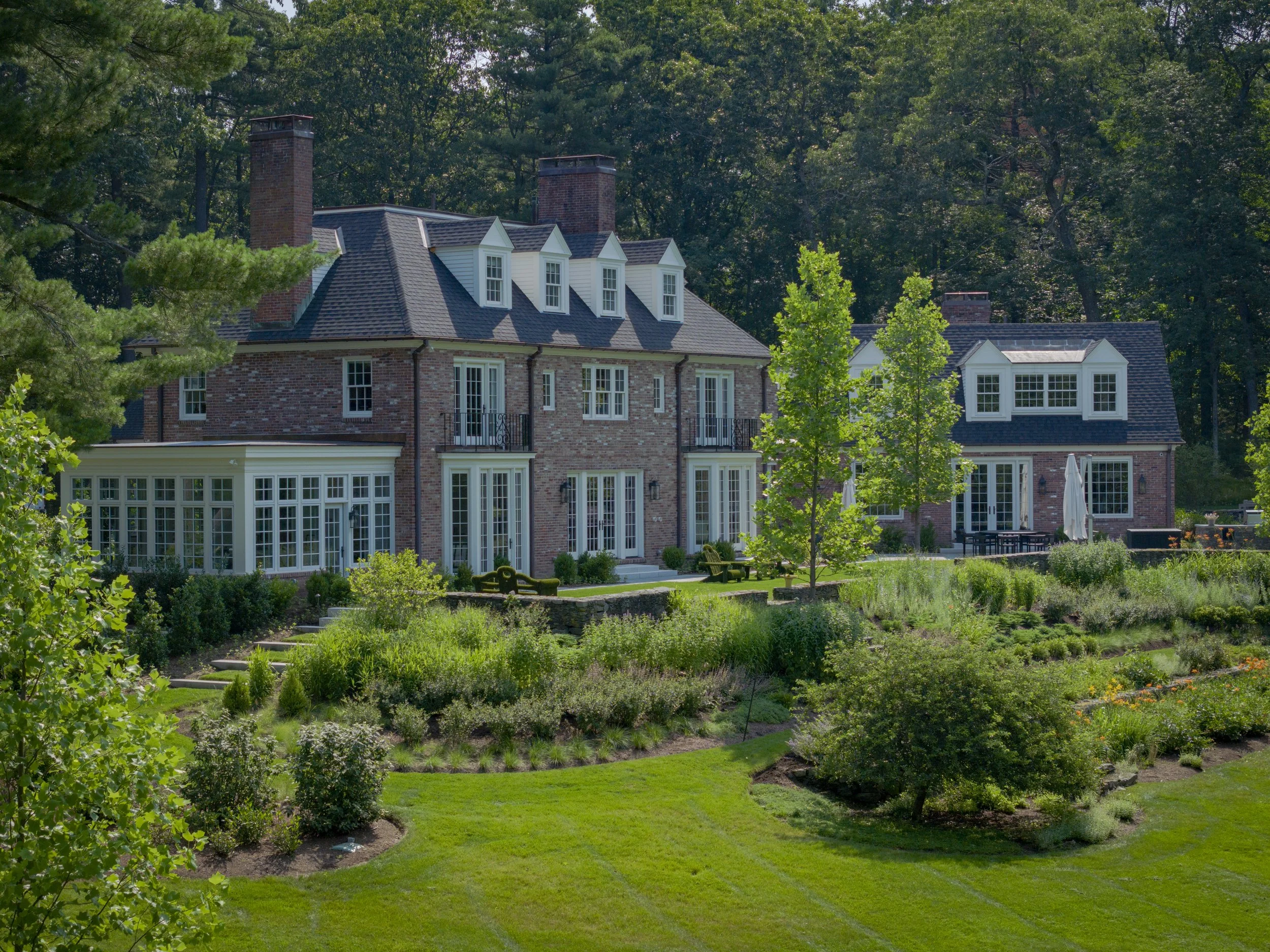 Large brick house with white window frames and multiple chimneys, surrounded by well-maintained garden and trees.