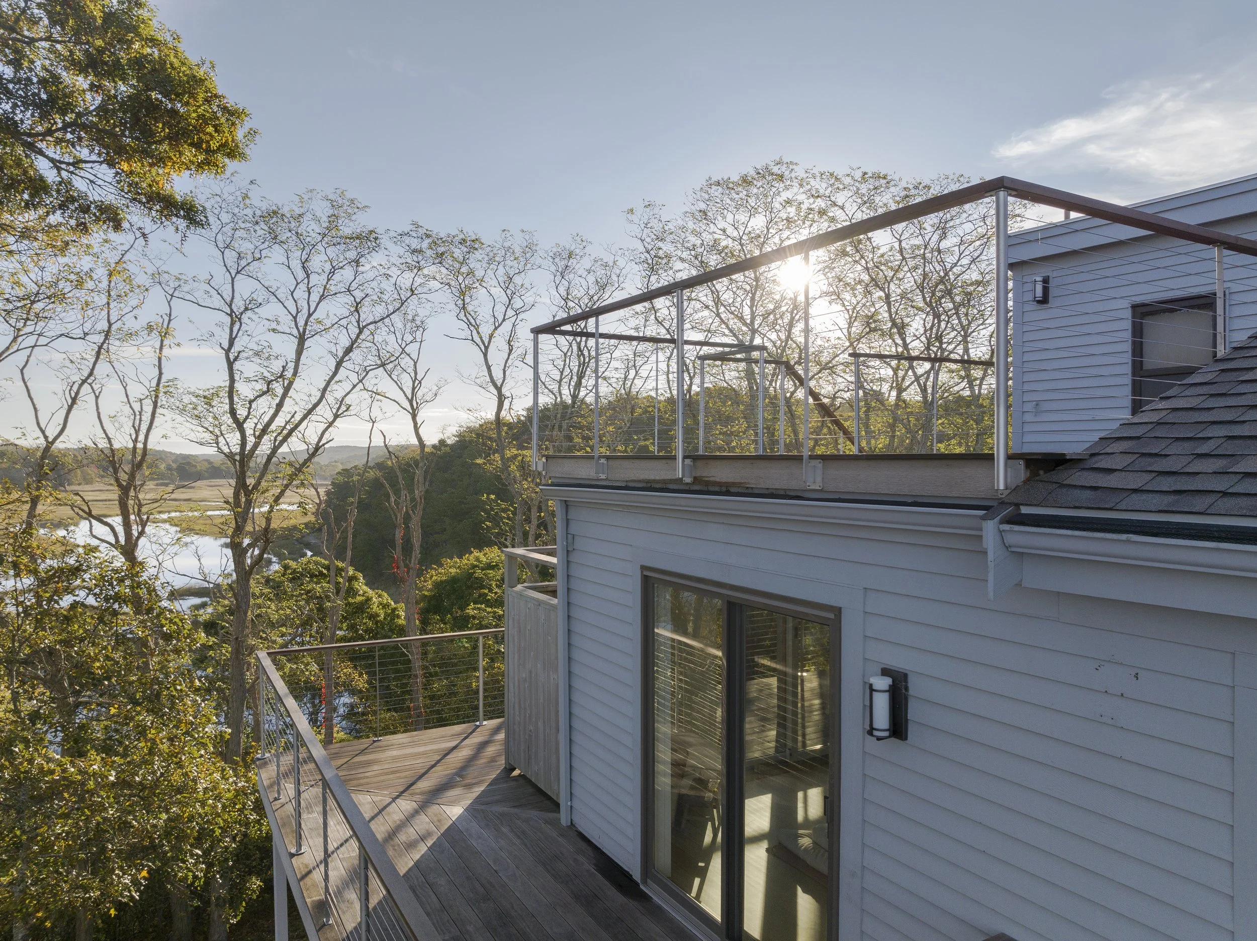 A view from a house's balcony showing trees, a river, and the sun shining through the branches.