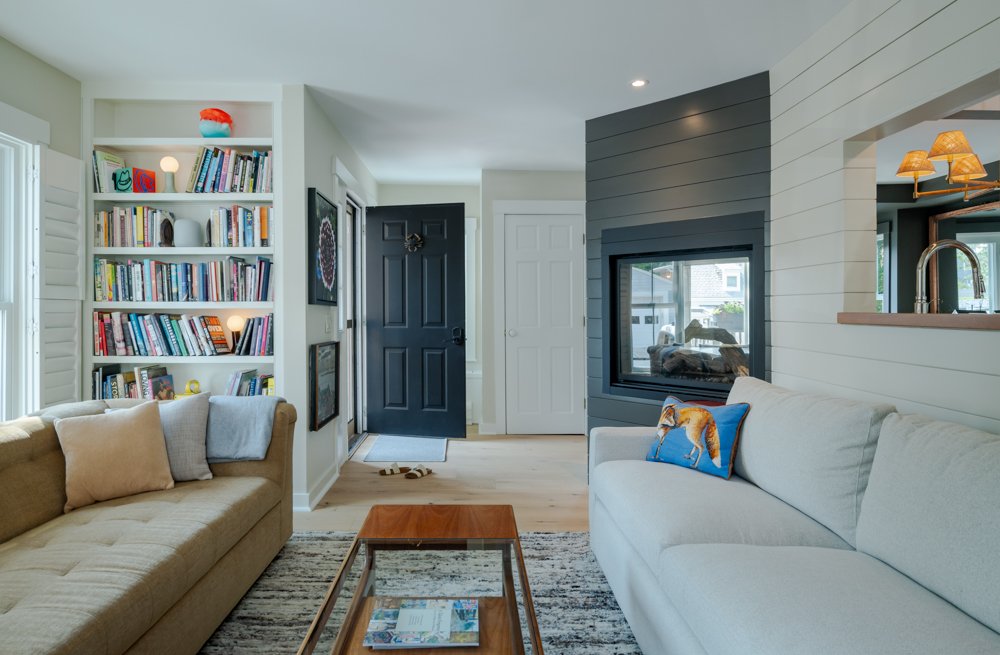 Living room with two couches, one beige and one white, a wooden coffee table, a bookshelf filled with books, and a fireplace built into the wall.