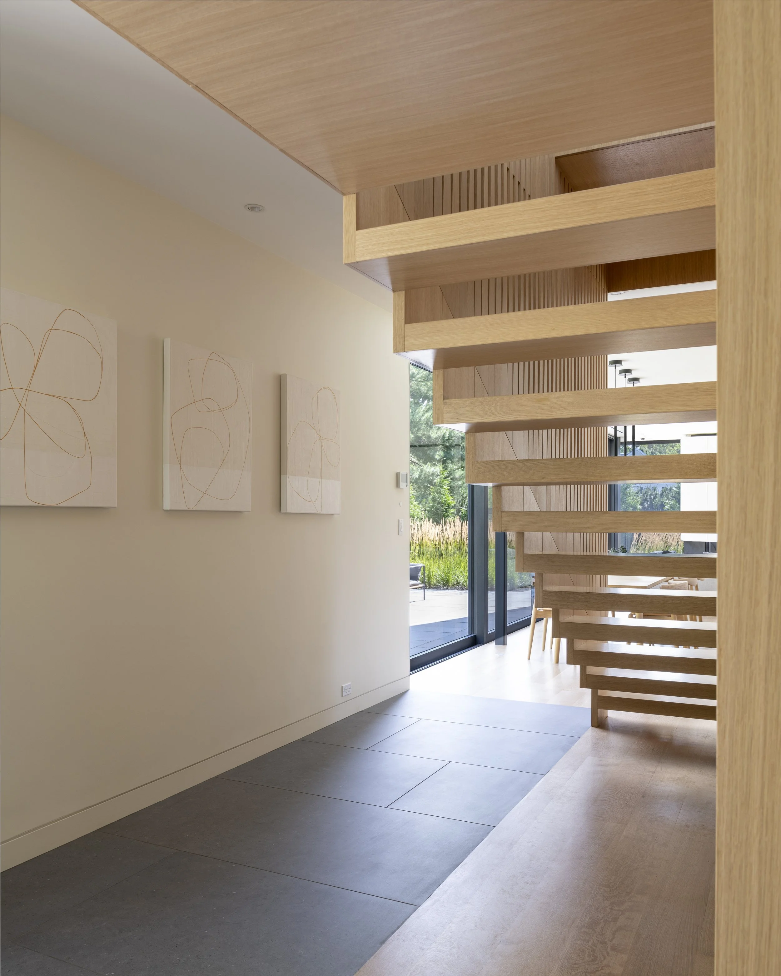 Modern interior hallway with a wooden staircase, large sliding glass doors, and abstract wall art.