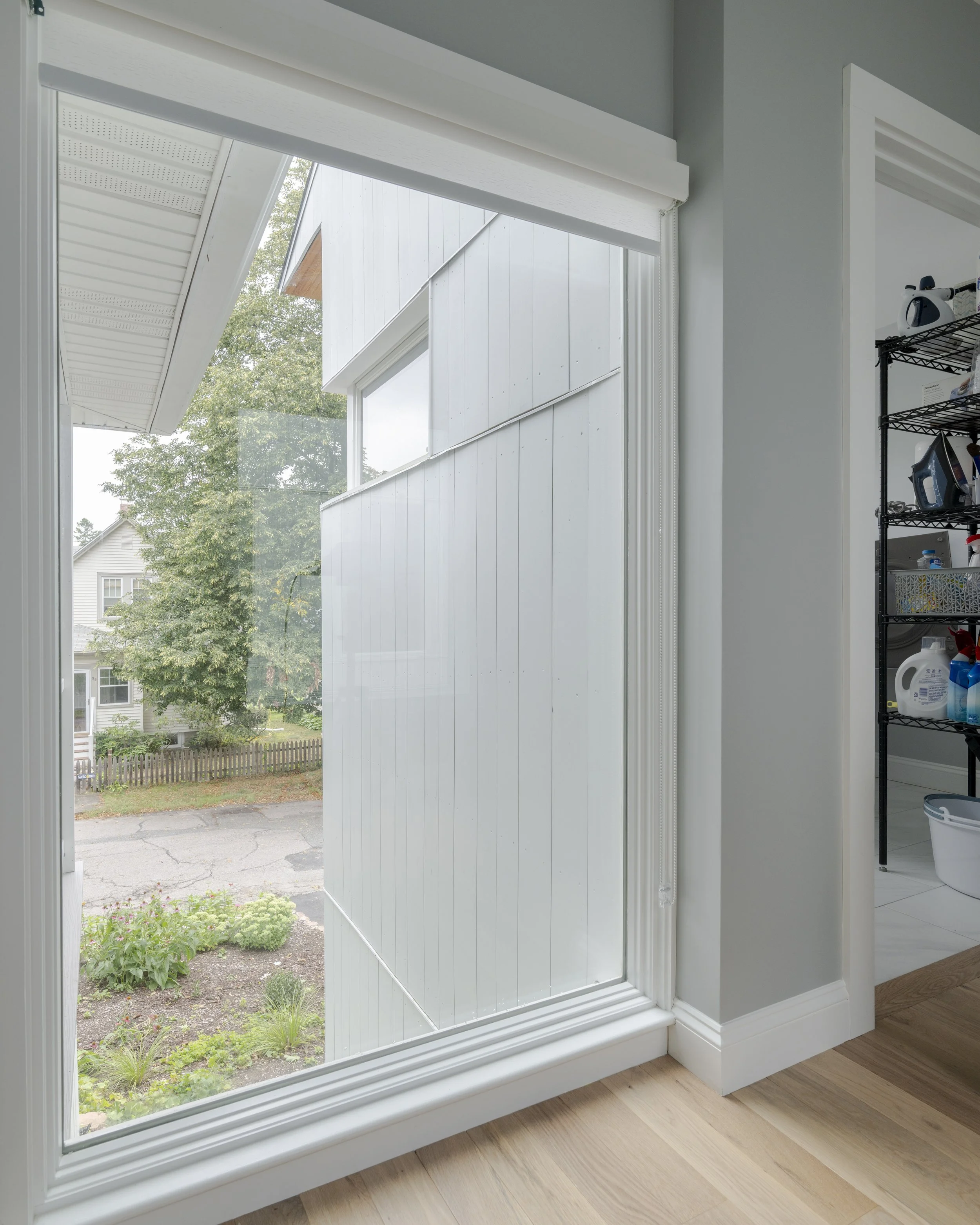 View from inside a house looking out a large glass sliding door, showing a garden, trees, and neighboring houses outside.