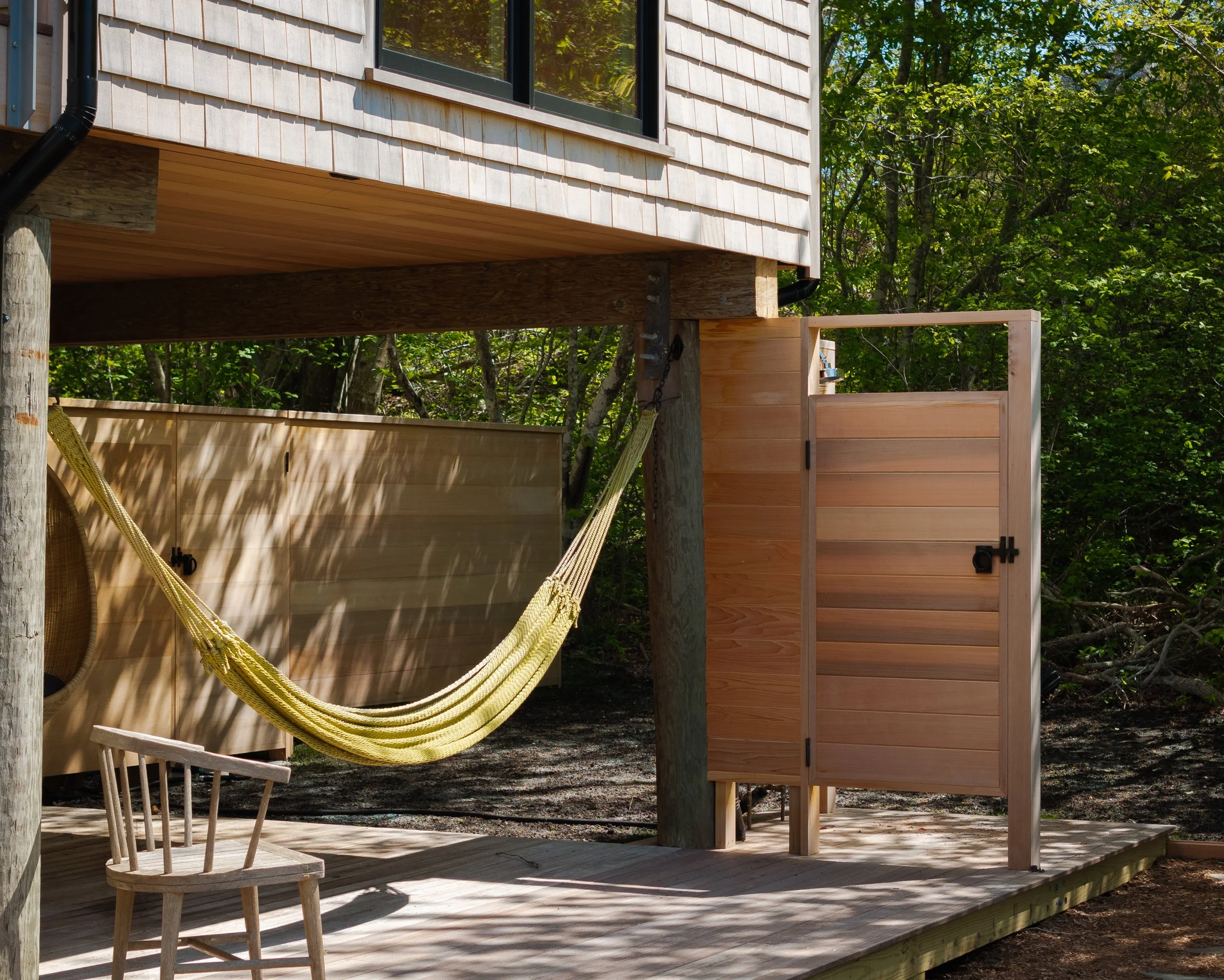 Wooden deck with a hammock, a small wooden chair, and a privacy screen, surrounded by trees and green foliage.