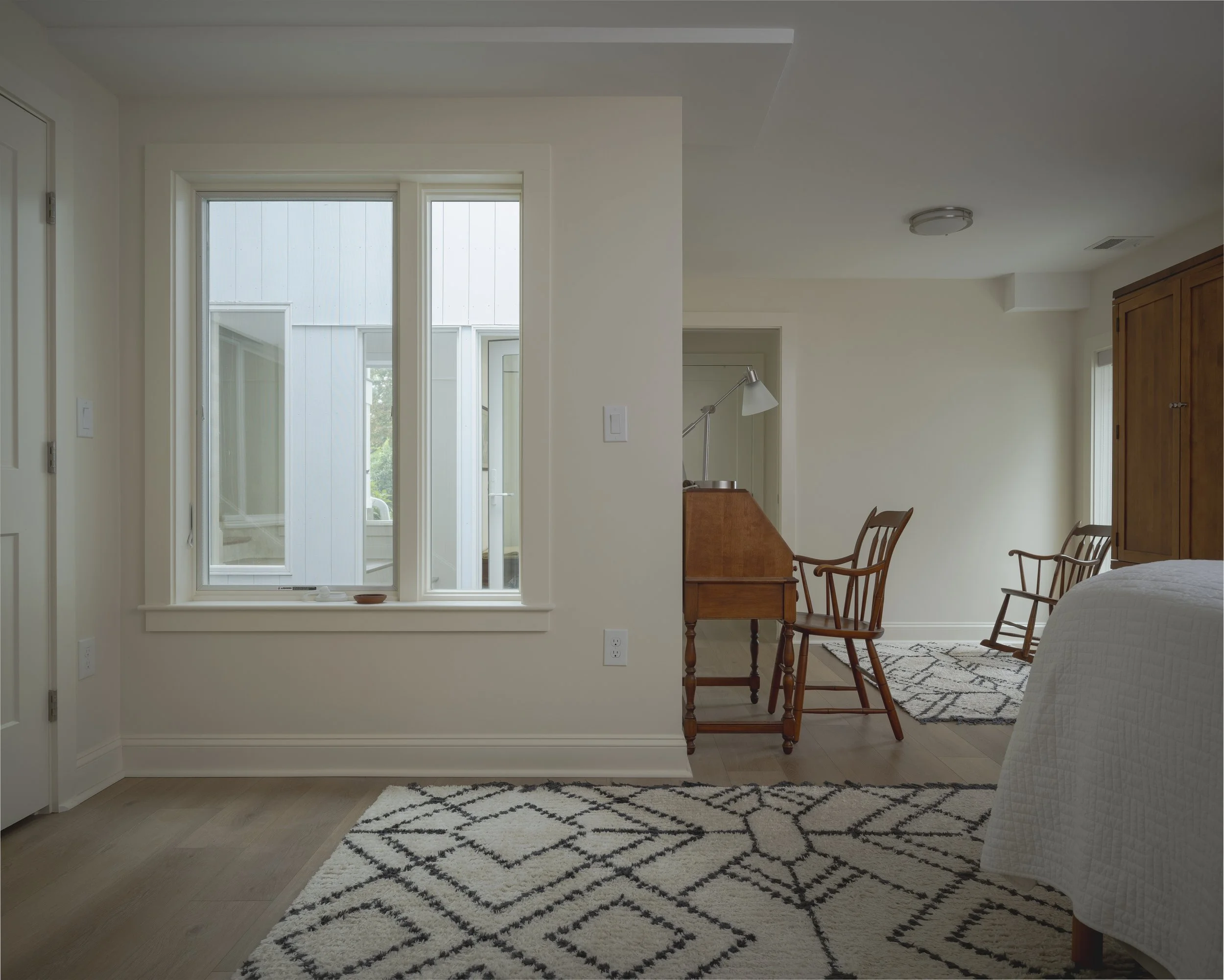 A cozy bedroom with a bed, wooden furniture, a window displaying an outdoor scene, and a small desk with a lamp.
