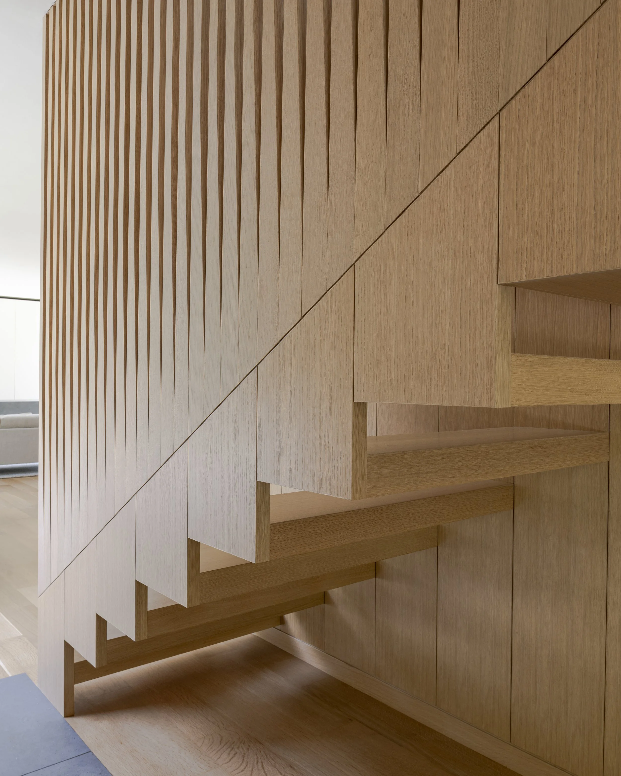 Wooden staircase with a modern, minimalist design and vertical slats on the side, inside a house.