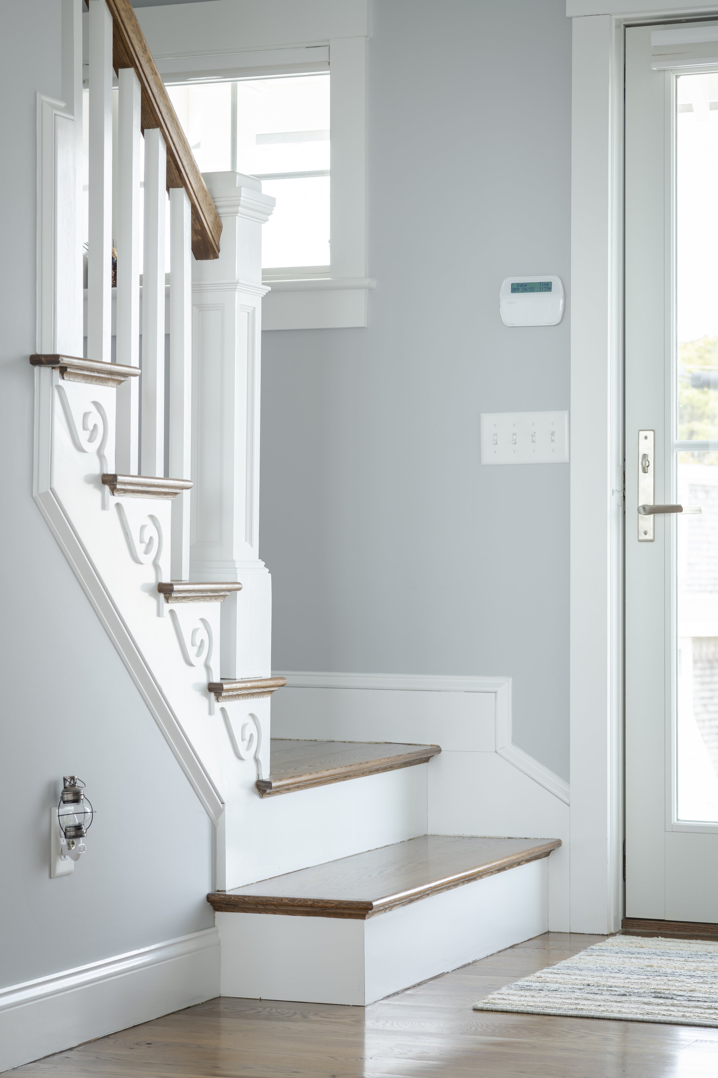 Interior view of a home entryway with stairs, a door, a thermostat on the wall, and a rug on the floor.