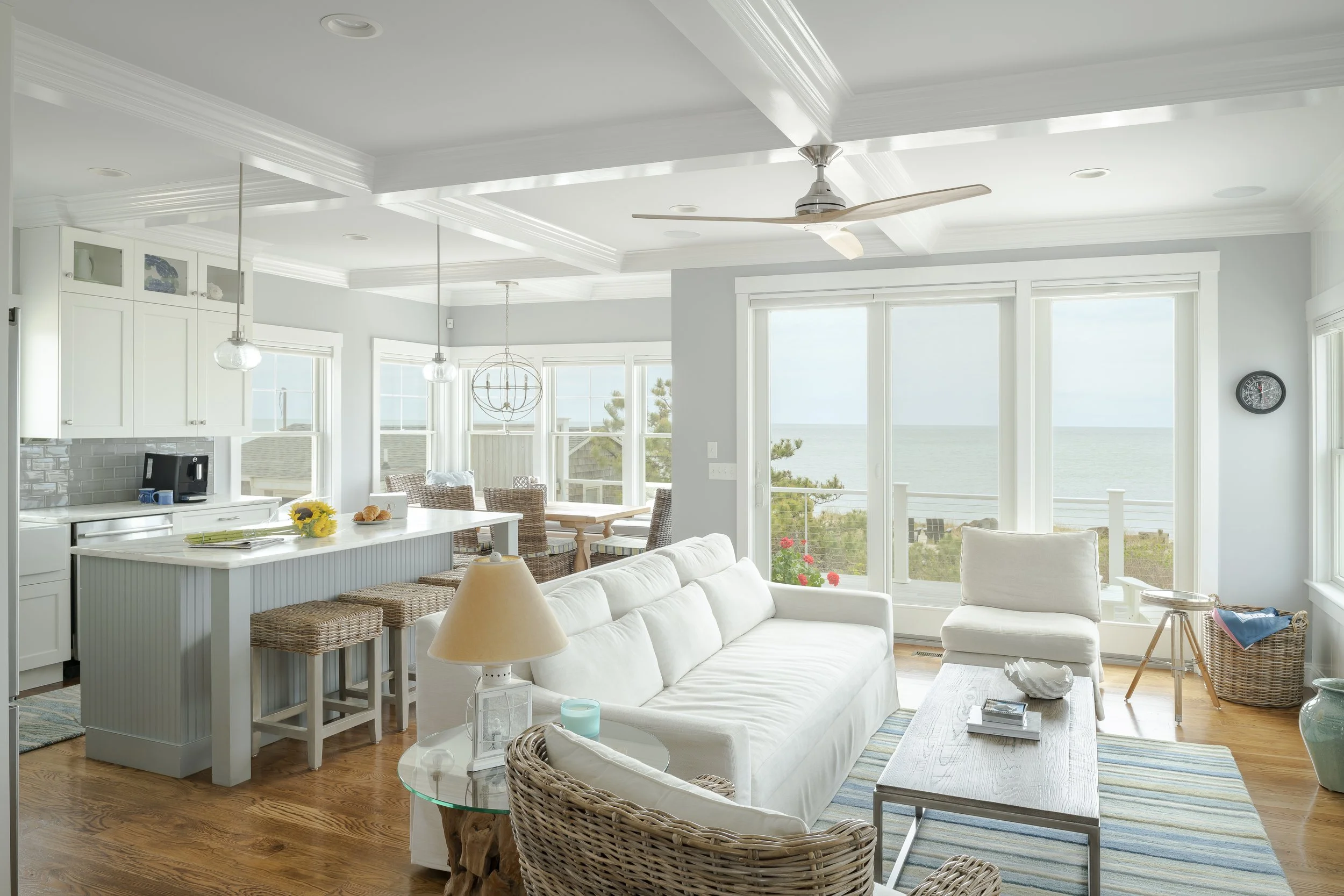 Living room with white furniture and panoramic ocean views through large windows.