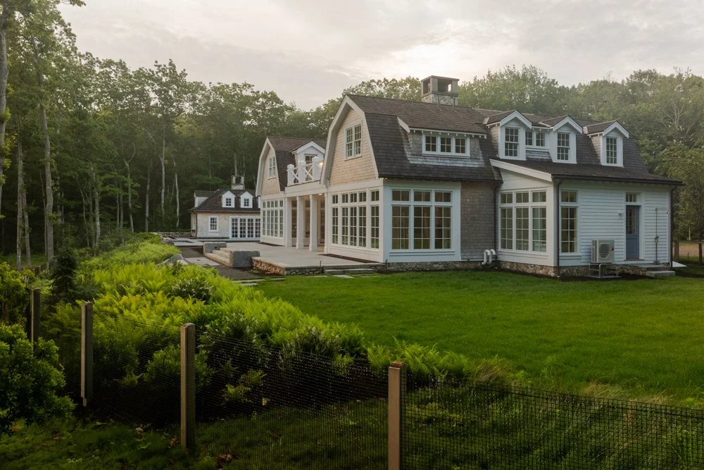 Large modern house with multiple windows and a spacious lawn, surrounded by trees.