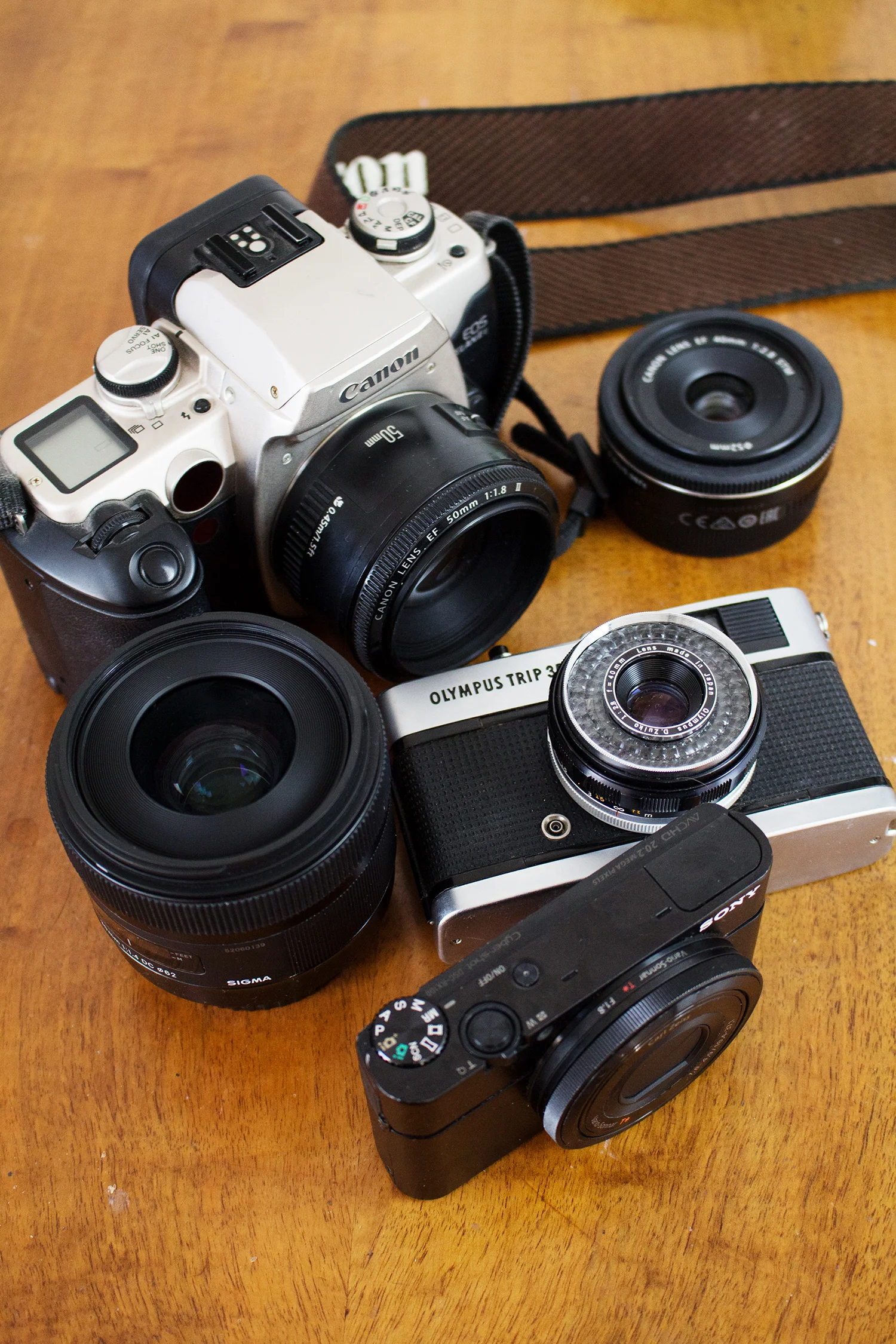 Canon 50E SLR, Olympus Trip 35, Sony RX100 and lenses on desk. Photography by Alice Red.