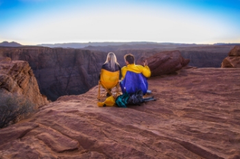 A couple sits on the edge of the lookout to enjoy the sunset at Horseshoe Bend with a bottle of wine and some cigars. Others bring a blanket to sit and enjoy the moment.