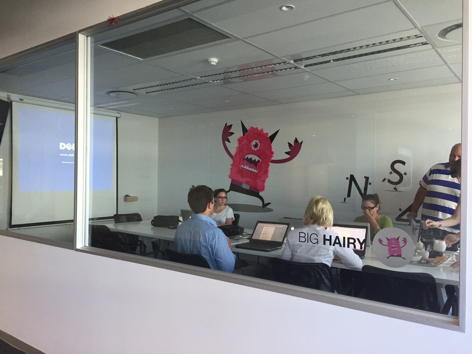 The Big Hairy meeting room describes our big hairy audacious goal, which is to have more impact than UNISA by 2024. The room has the big, angry GetSmarter monster chasing after a jumbled up UNISA running away in the right of the image.
