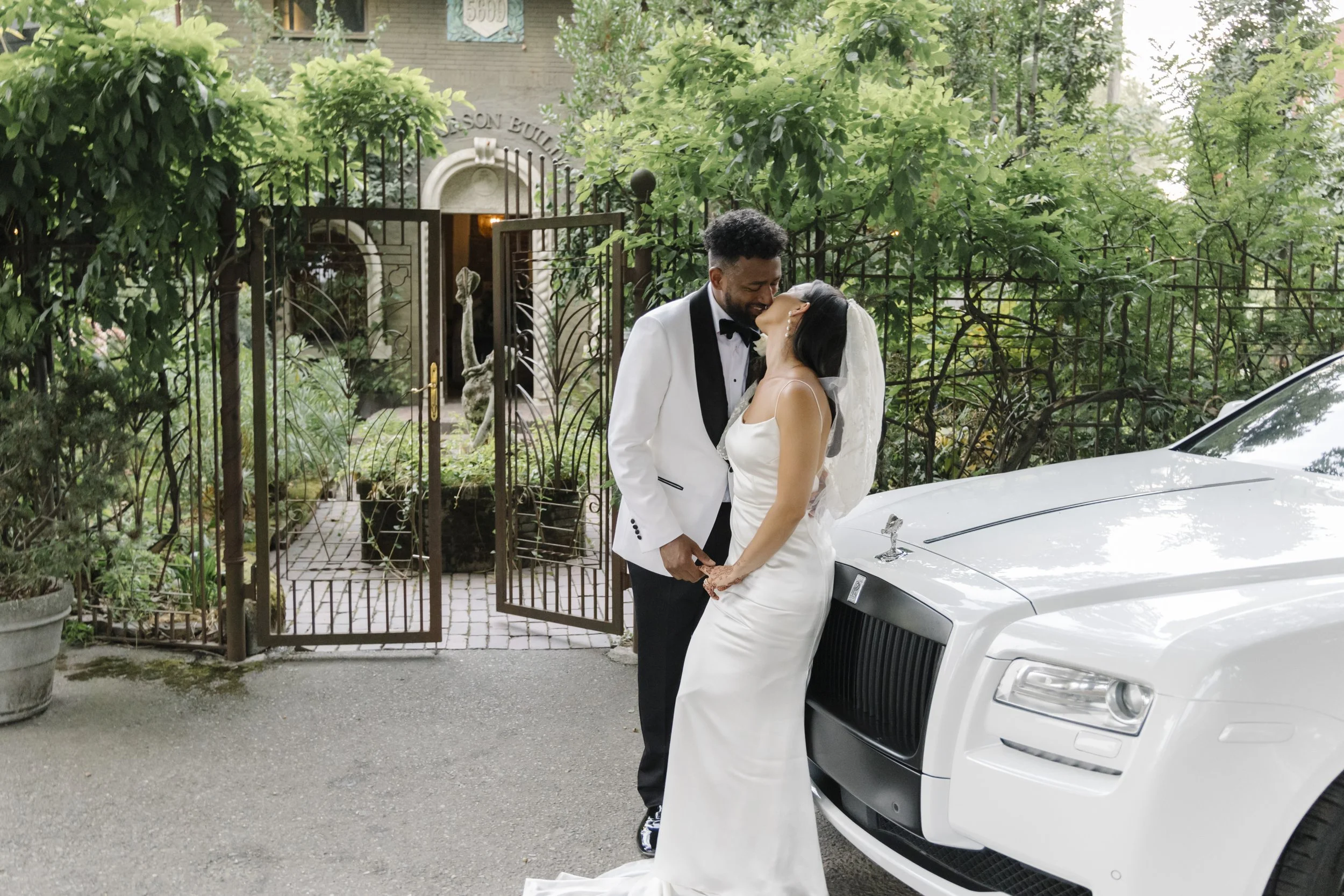 The Corson Building wedding with a bride wearing a lace cape, and a groom in a white tuxedo in front of a Rolls Royce.