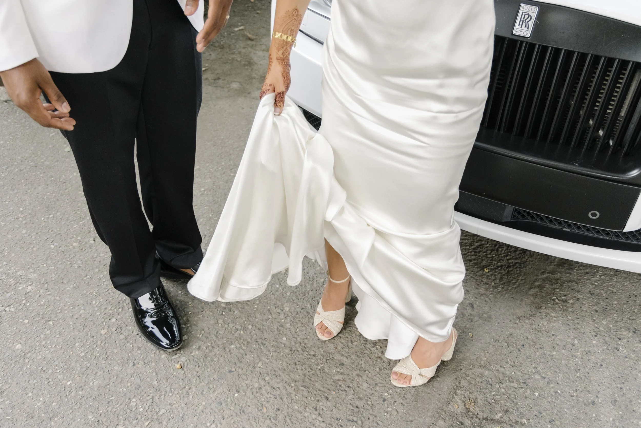 The Corson Building wedding with a bride wearing a lace cape, and a groom in a white tuxedo in front of a Rolls Royce.