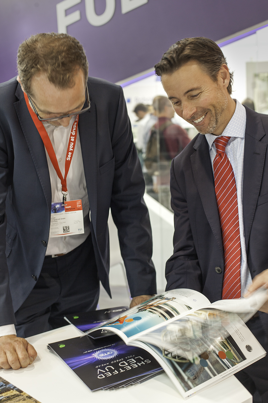 AMS president Steve Metcalf (right) flips through the LED Look Book at drupa 2016; this print piece shows off the ever-expanding capabilities of LED-based curing in sheetfed offset printing applications.