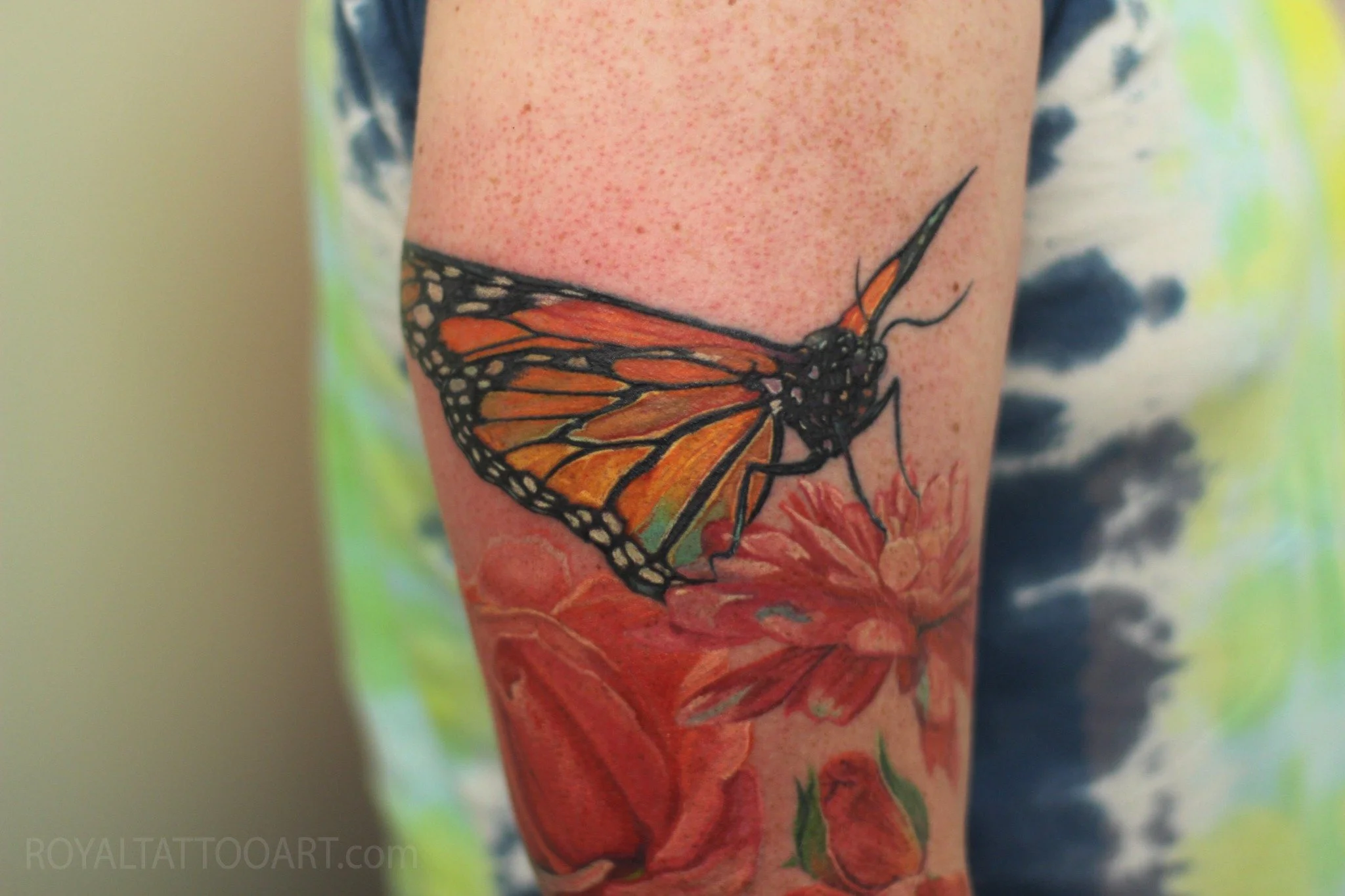 Color realism monarch butterfly tattoo with soft floral background, created with vivid orange wing detail and painterly color by Royal Jafarov at Royal Tattoo Art in NYC.