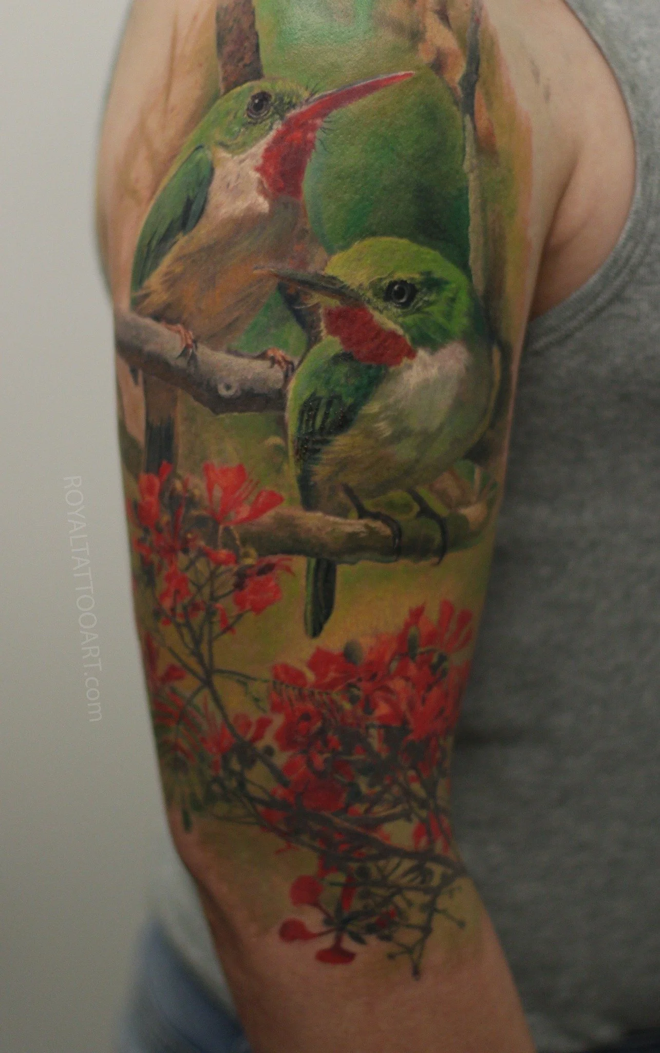 A detailed color realism tattoo on the thigh features a small bird perched among lush greenery and vibrant red flowers, creating a naturalistic scene.