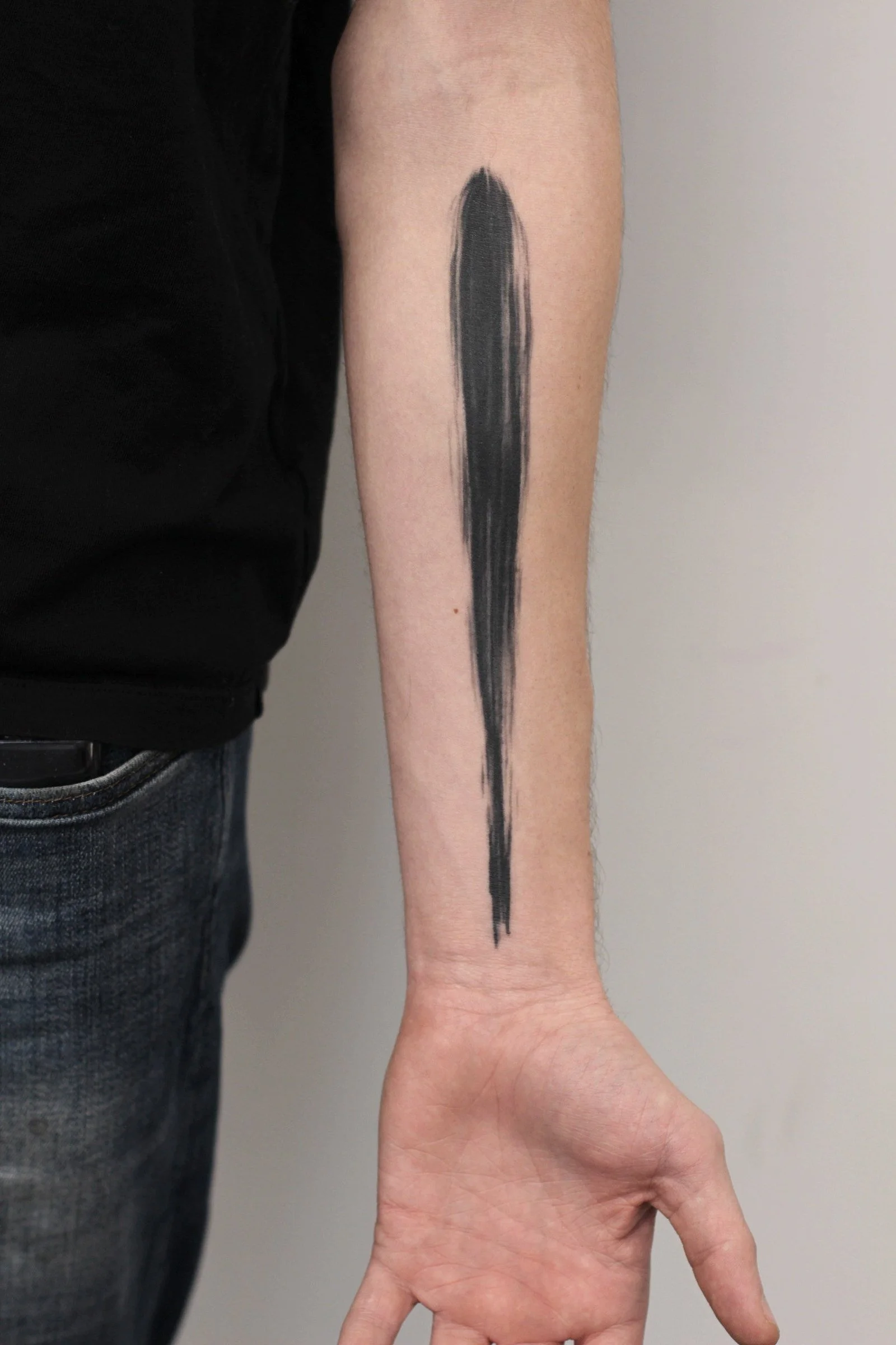 Minimalist single bold black brushstroke tattoo down the forearm, clean abstract ink design by Royal Jafarov at Royal Tattoo Art