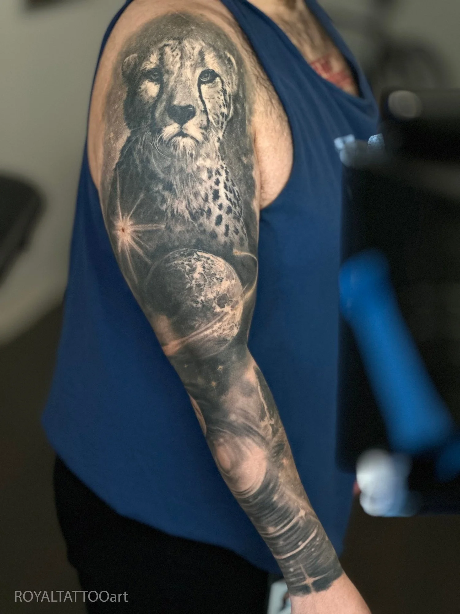 Black and grey realism sleeve tattoo featuring a cheetah portrait with space and planetary elements in a custom surreal composition.
