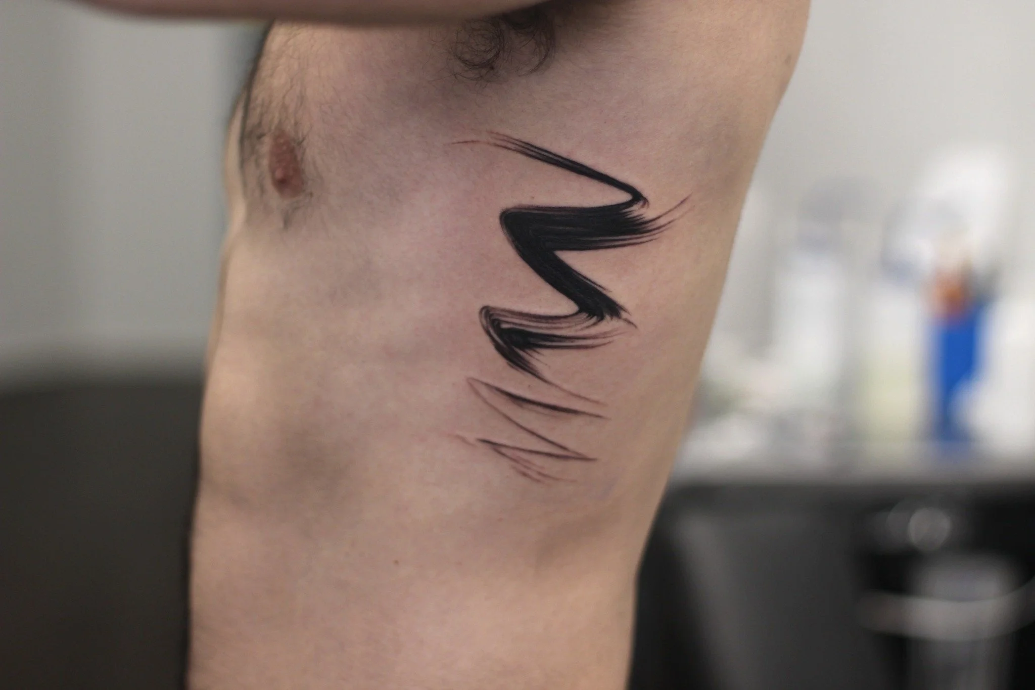 Minimalist abstract black brushstroke tattoo on ribs, bold lightning bolt ink design by Royal Jafarov at Royal Tattoo Art