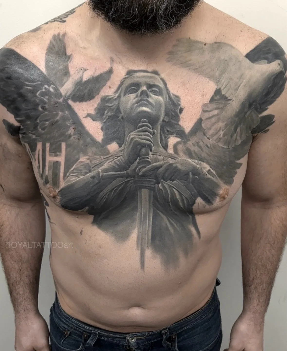 Joan of Arc Black and Grey Realism Chest Tattoo – A powerful full chest piece depicting Joan of Arc as a warrior saint, rendered in stunning black and grey realism. The composition features angelic wings, a sword, and dramatic shading by Royal Jafaro