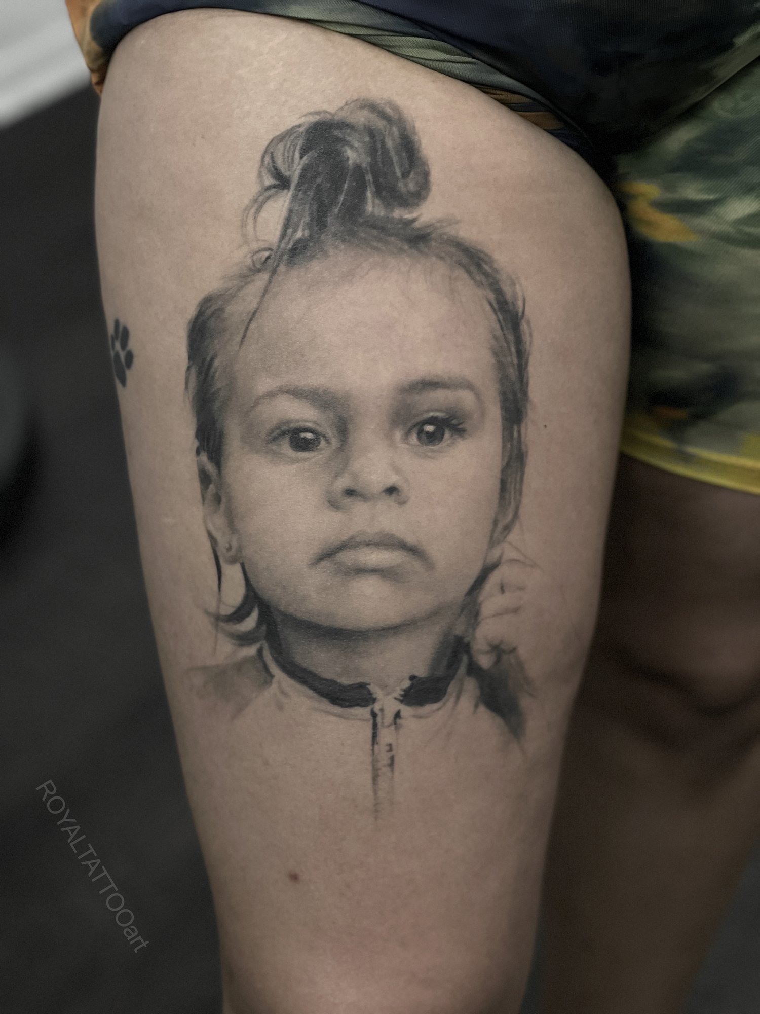 Child Portrait Thigh Tattoo in Black and Grey Realism – A tender and lifelike child portrait tattoo placed on the thigh, rendered in black and grey realism. The delicate skin tones and facial expression are beautifully preserved in ink by Royal Jafar