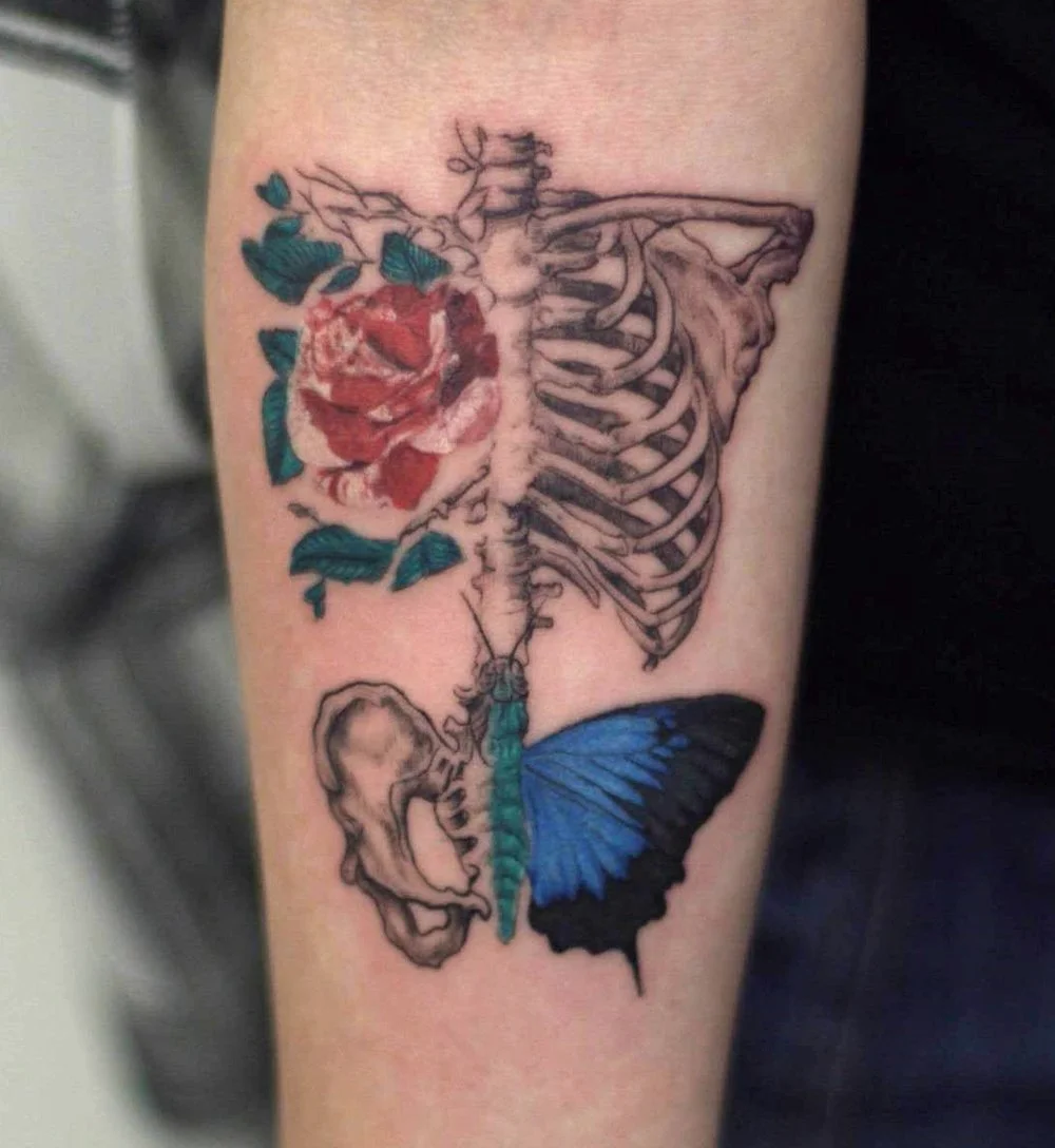Color micro realism tattoo of an anatomical ribcage adorned with red roses and a blue butterfly, blending realism with delicate linework, by Royal Jafarov at Royal Tattoo Art in NYC.