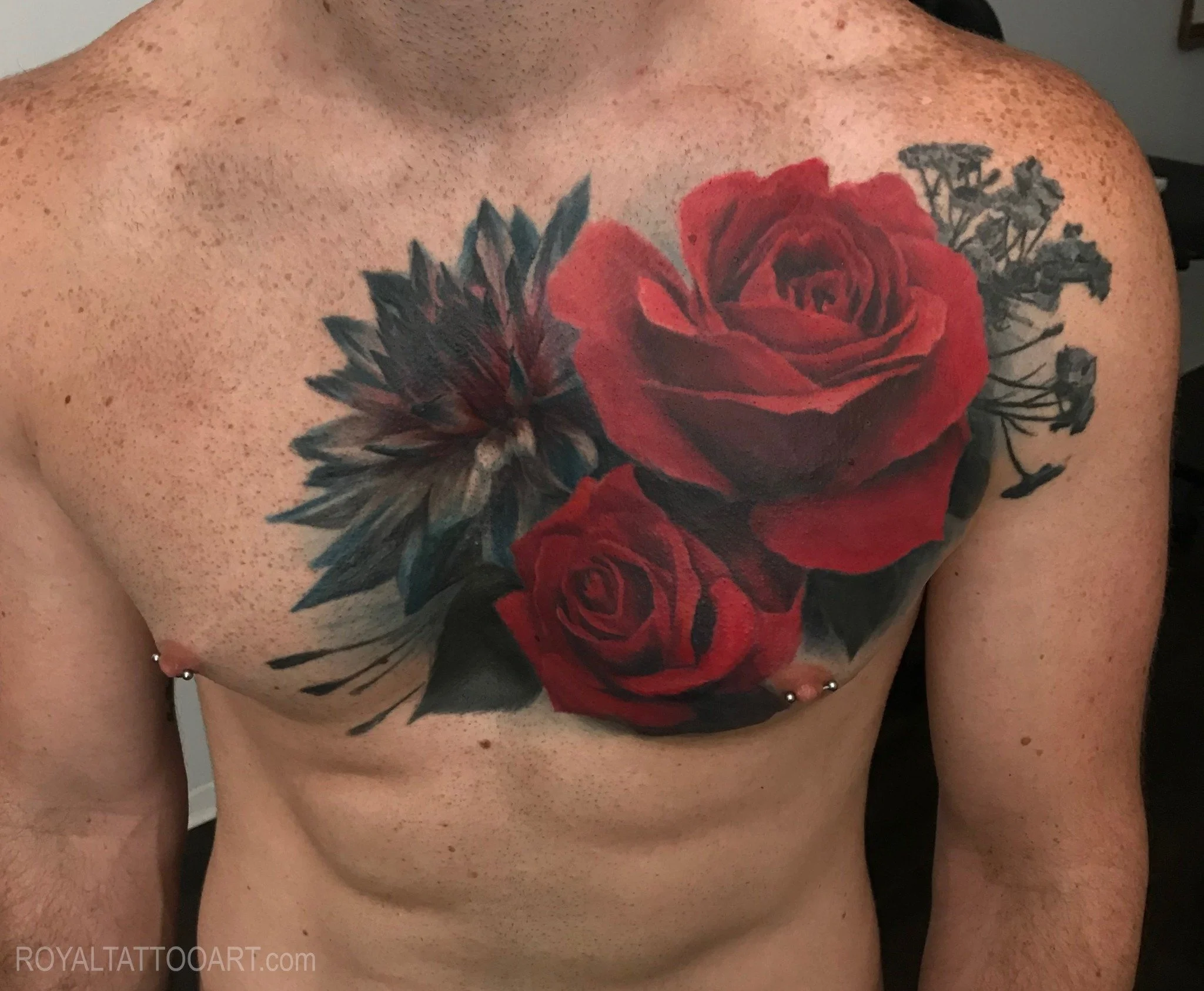 A large chest tattoo featuring a cluster of realistic red roses with dark green leaves, rendered in rich color realism.